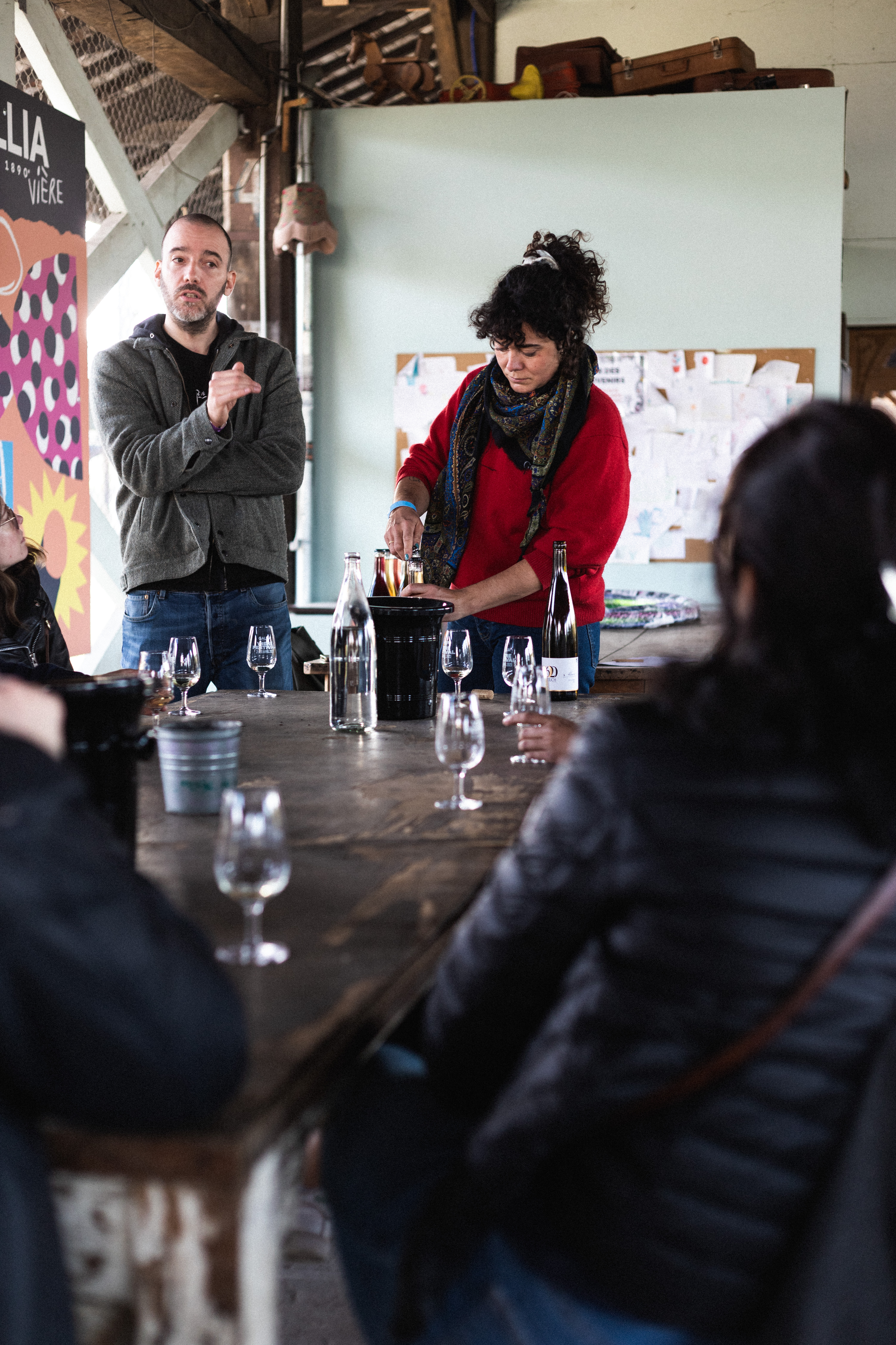 Céline Maguet qui débouche une bouteille derrière une table, avec des gens autours qui la regardent.