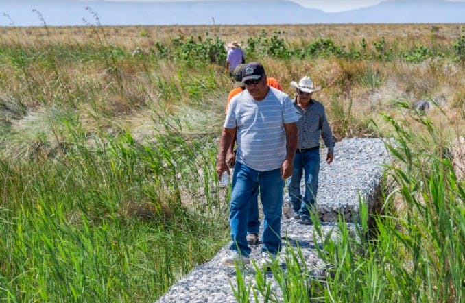 Ejidatarios caminan sobre una presa de gaviones que ha quedado en el desierto y sin agua.