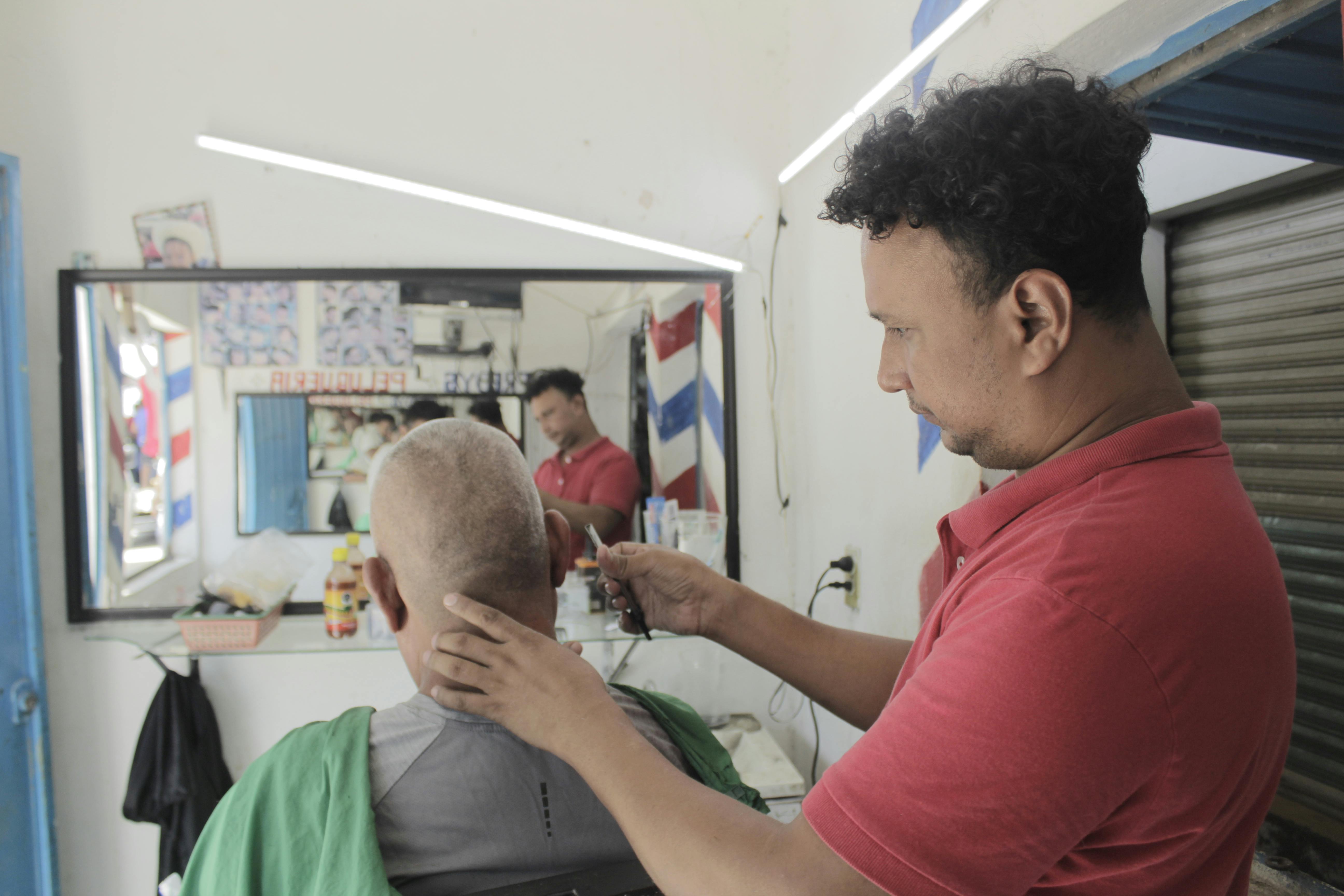 Un hombre originario de honduras le corta el cabello a otro mexicano
