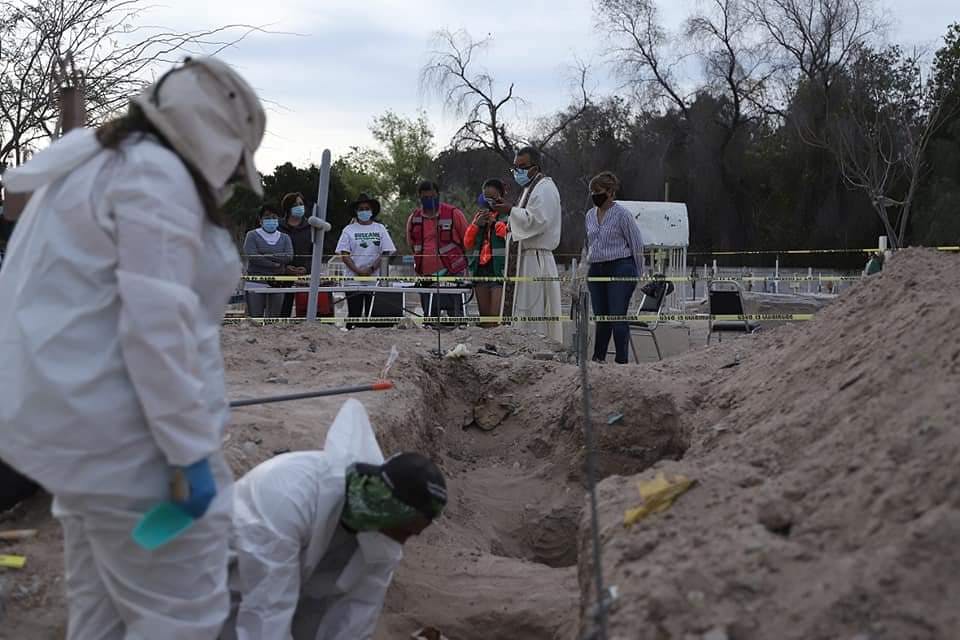 Expertos forenses realizan una exhumación, mientras las familias rezan con un cura en la parte del fondo de la imagen. Desaparecidos, Coahuila.