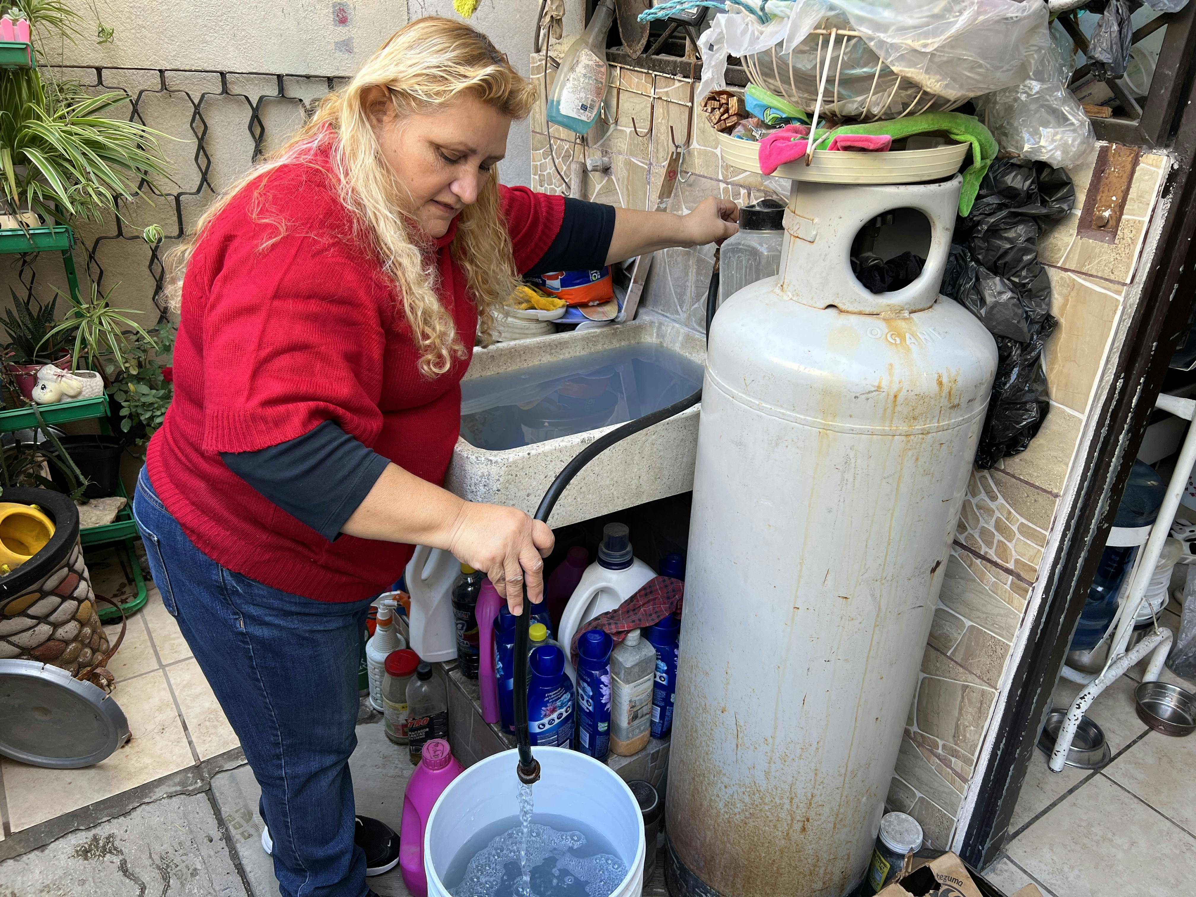 Diana Obregón con camisa roja, echa agua en un contenedor 
