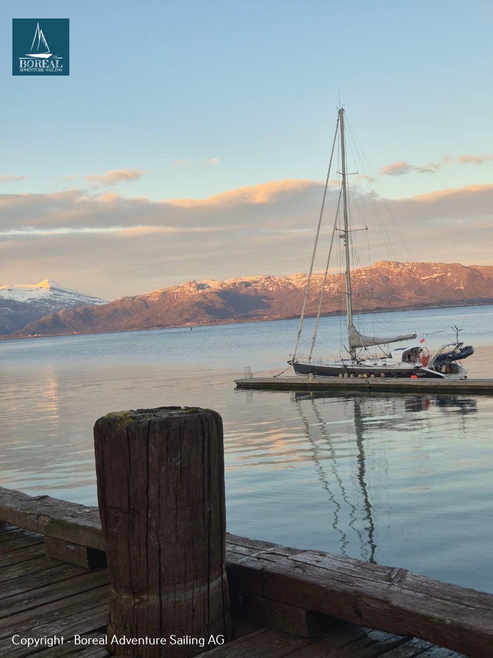 Offshore Sailing: yacht moored at a calm fjord jetty beneath pink-lit mountains