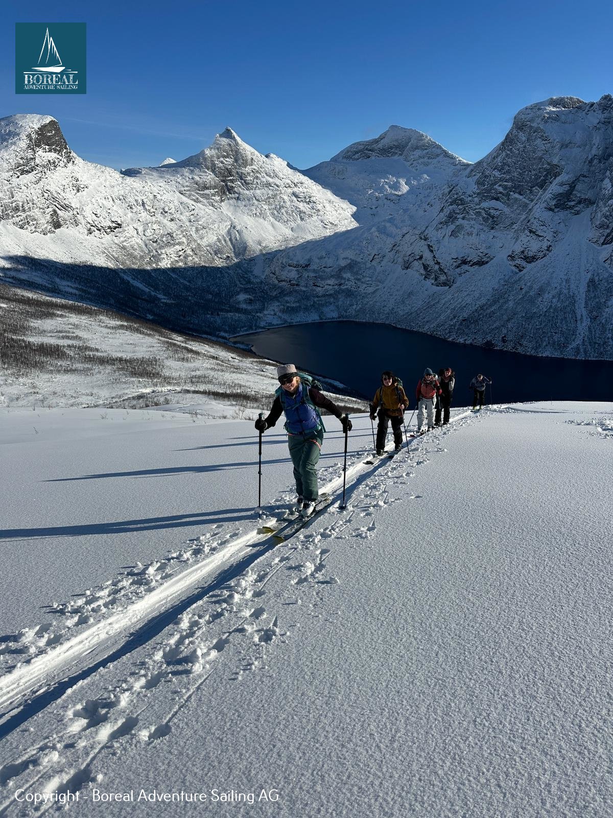 Ski & Sail, Bodø & Lofoten: ski tourers skinning uphill in a line, jagged peaks behind