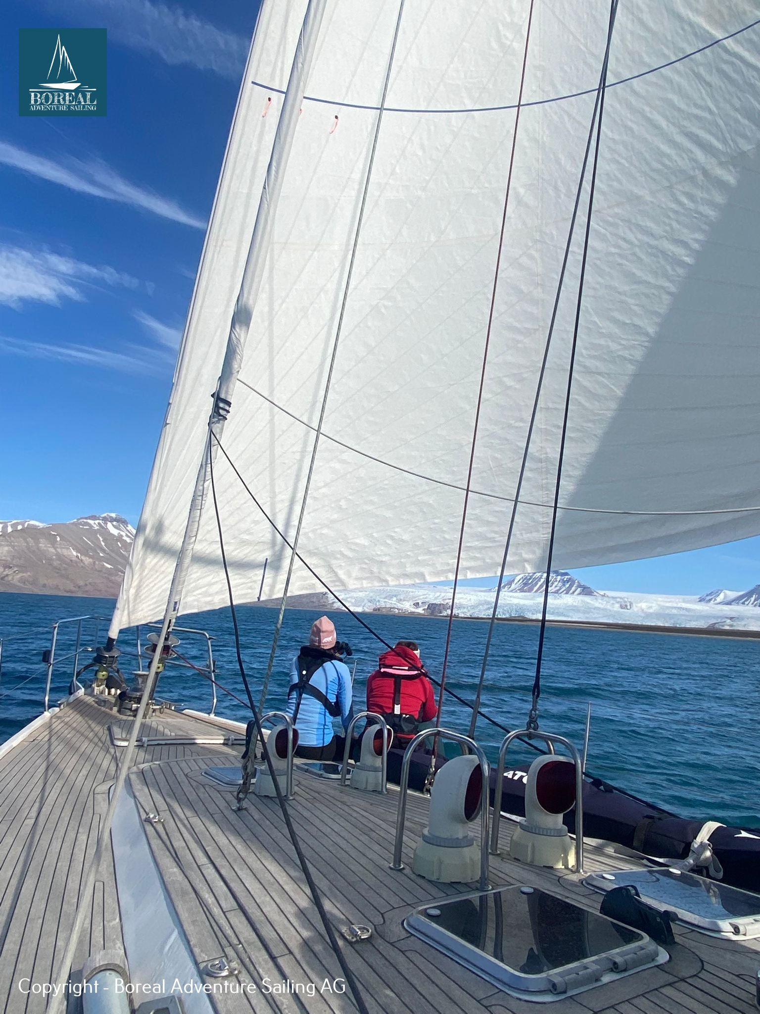 Sail & Explore, Svalbard: guests on deck beneath a big white sail, sailing in sunshine