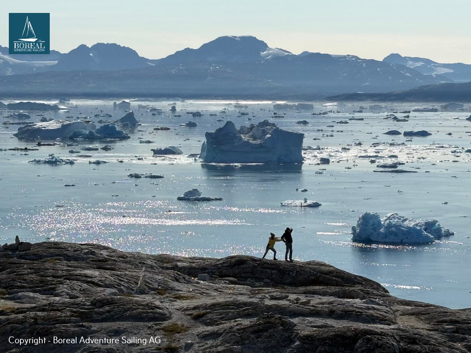 Sail & Explore, East Greenland: two hikers on a rocky headland above an iceberg-filled bay