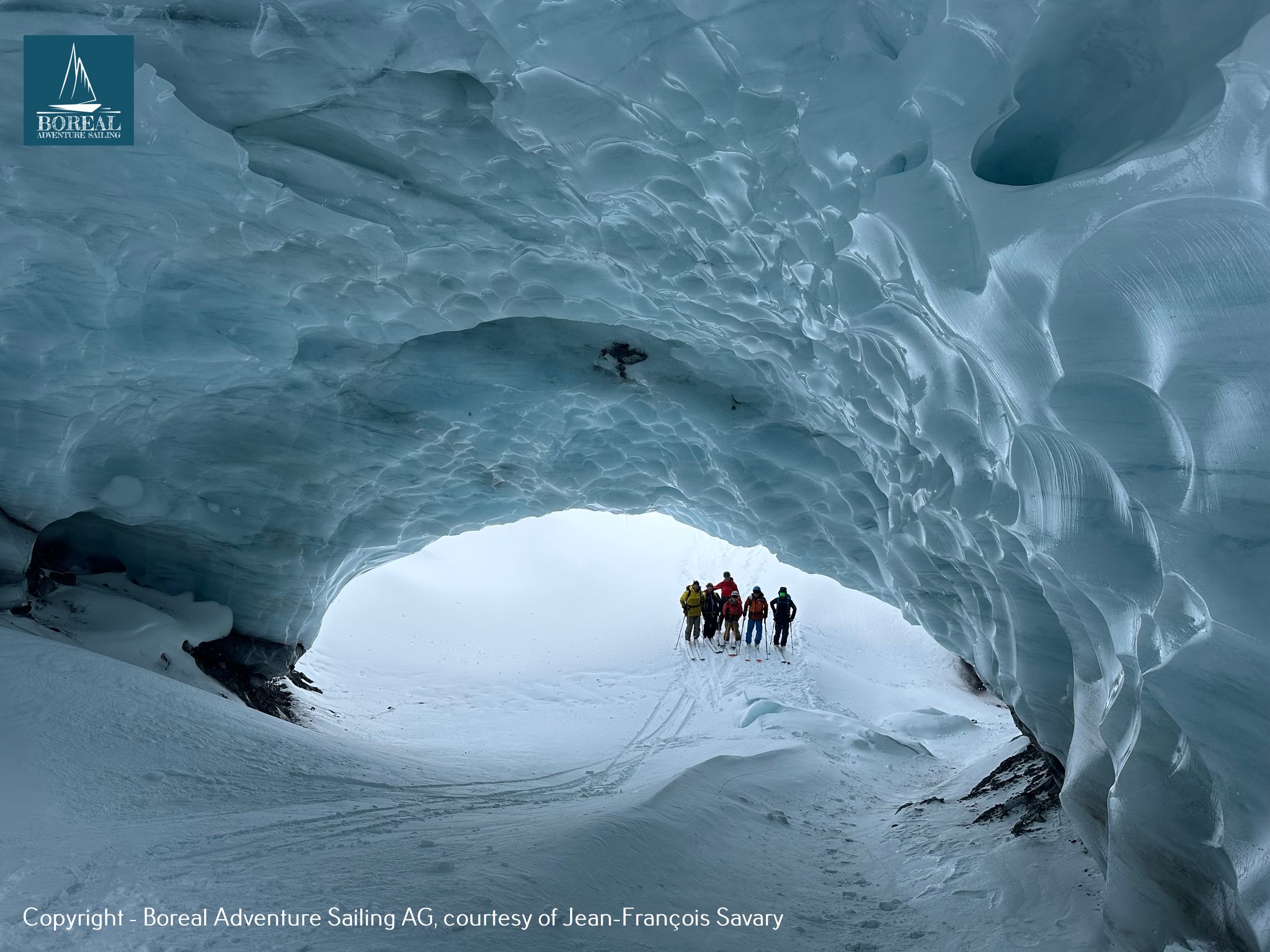 Ski & Sail, Svalbard: ski group framed by the arch of a glacier ice cave