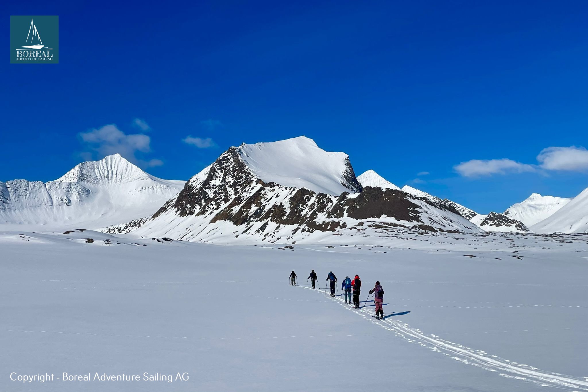 Ski & Sail, Svalbard: ski tourers skinning in line toward a jagged snowy peak