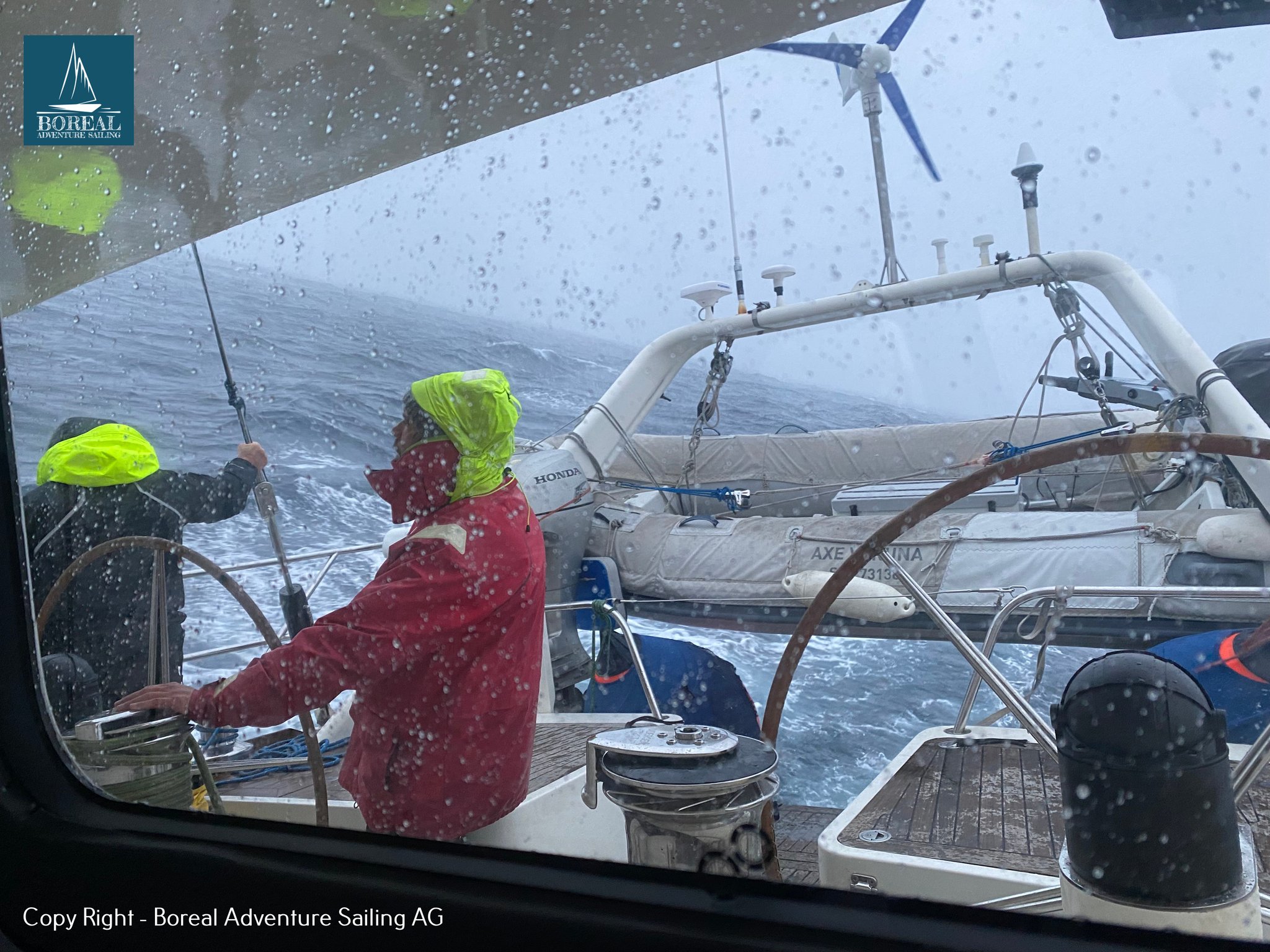 Offshore Sailing: helmsman in red foul-weather gear steering through rain and spray