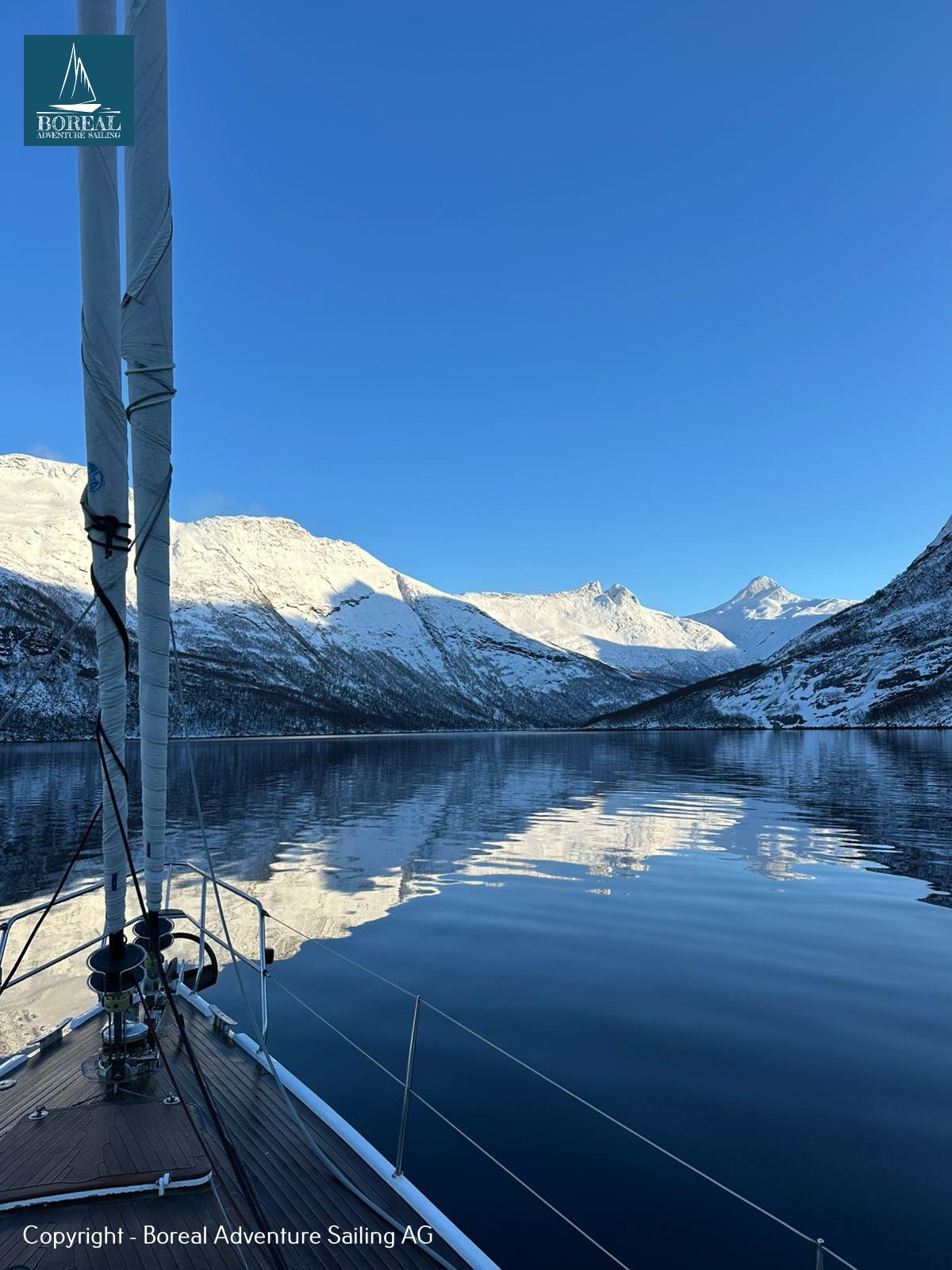 Ski & Sail, Bodø & Lofoten: view over the yacht's bow across a calm fjord and snowy mountains
