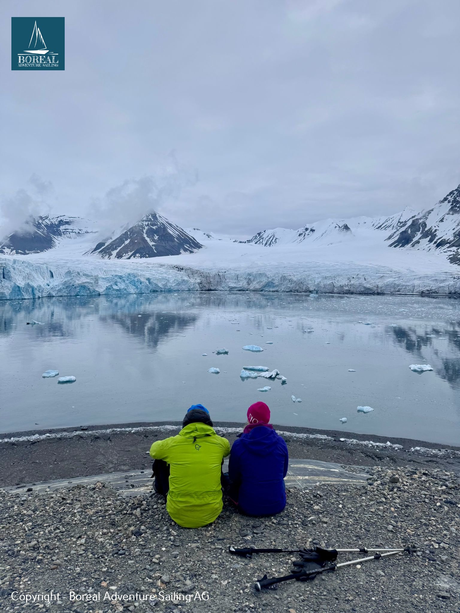 Sail & Explore, Svalbard: two guests on a beach contemplating a glacier reflected in calm water