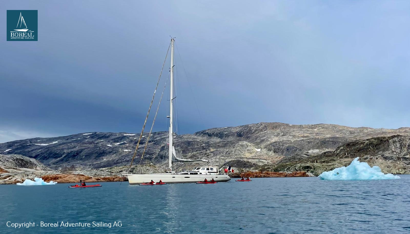 Sail & Kayak, East Greenland: anchored expedition yacht with red kayaks alongside and an iceberg
