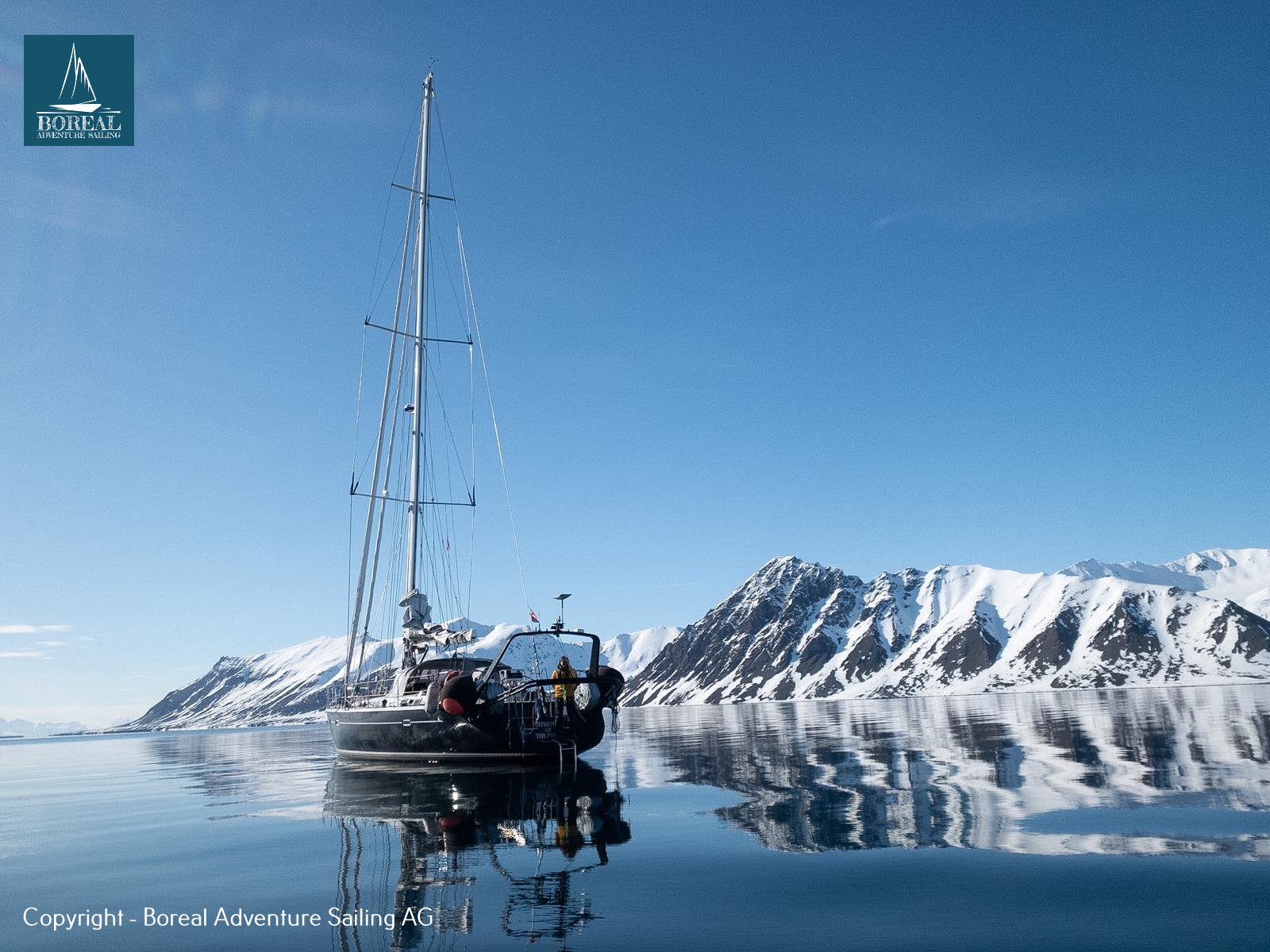 Ski & Sail, Svalbard: yacht at anchor below snowy peaks reflected in calm water