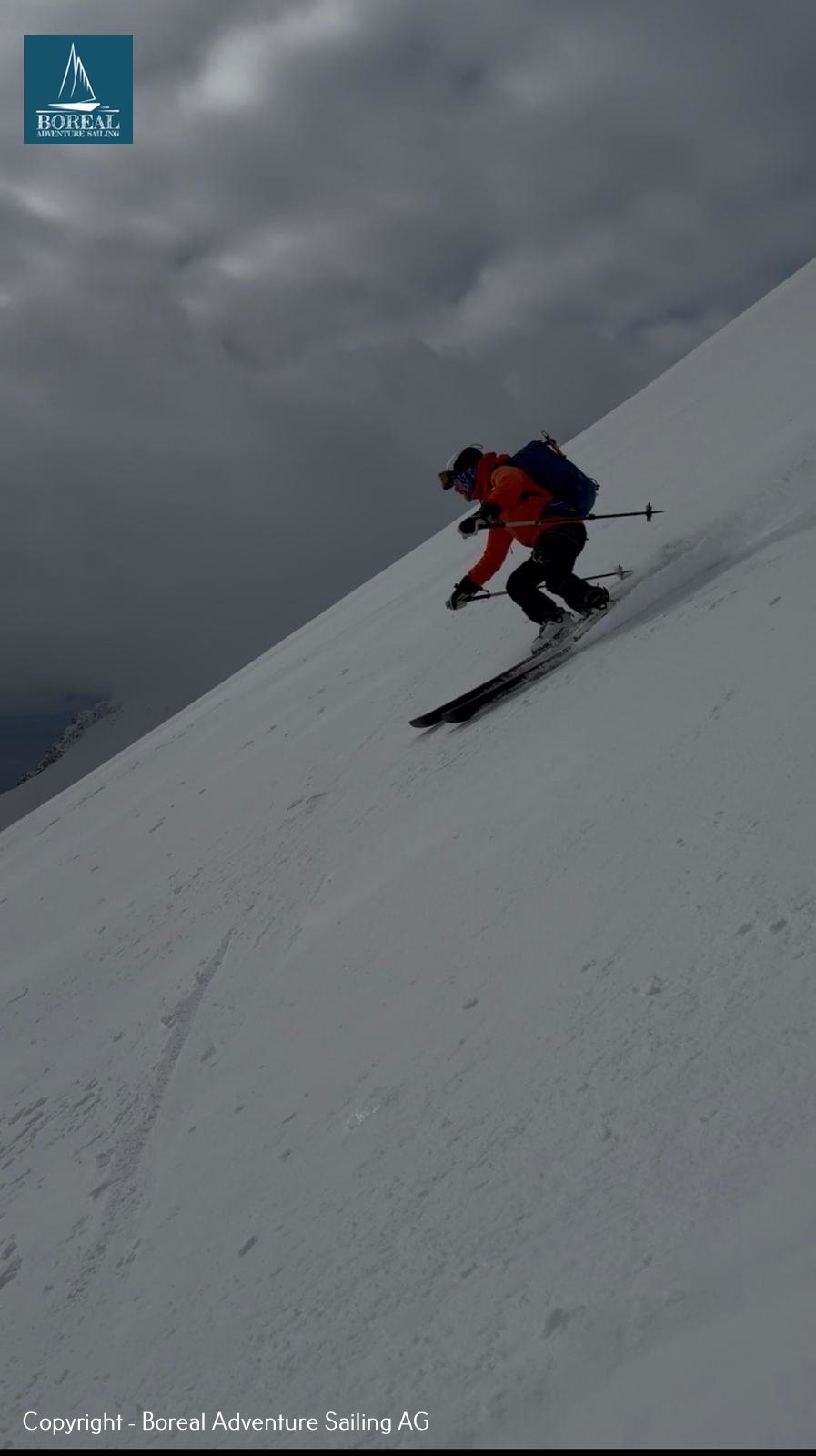 Ski & Sail, Svalbard: skier in red carving a steep slope under dark clouds