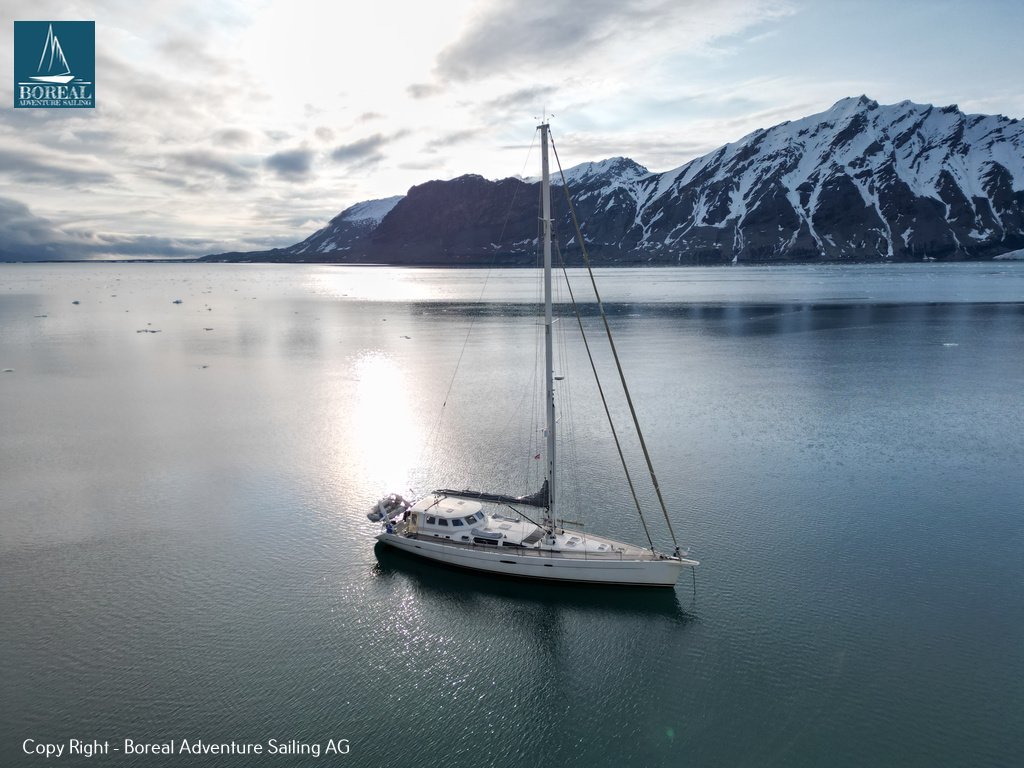 Sail & Kayak, Svalbard: drone view of the anchored yacht in a still, sunlit fjord