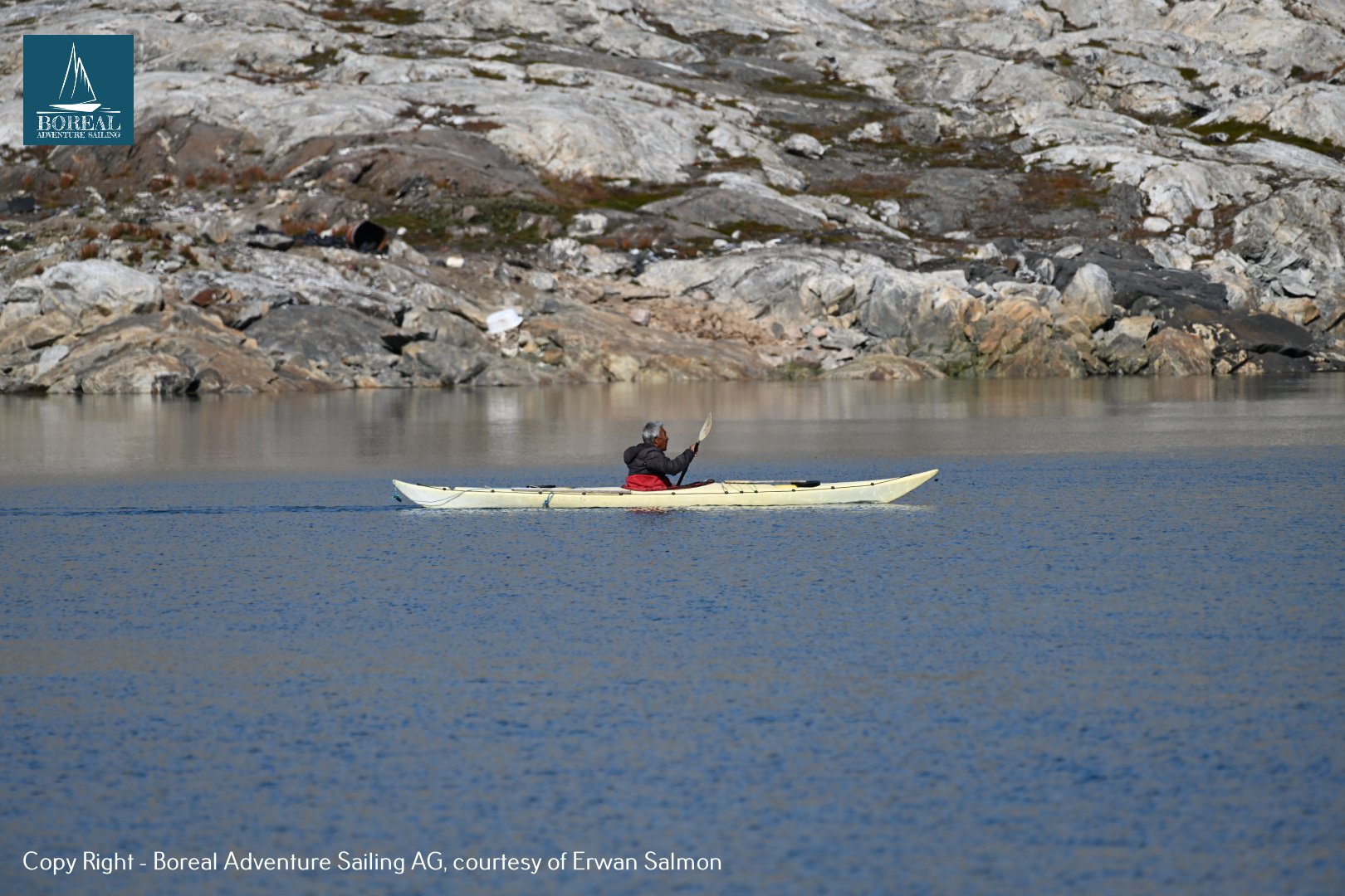 Sail & Kayak, East Greenland: lone paddler in a white sea kayak below rocky slopes