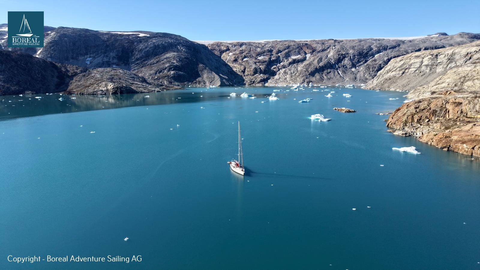 Sail & Explore, East Greenland: aerial view of the yacht anchored in an ice-dotted fjord