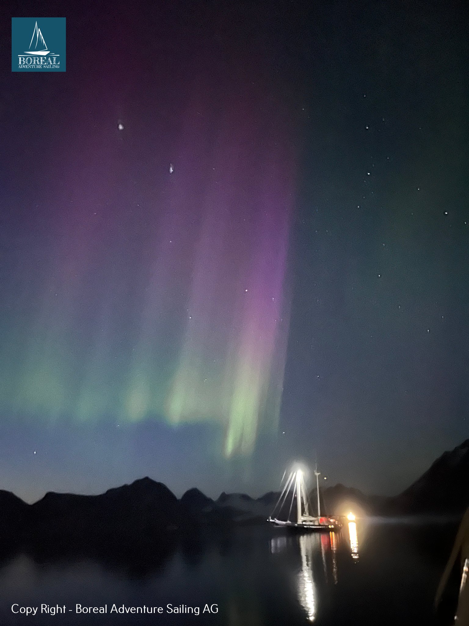Sail & Explore, East Greenland: northern lights glowing above the yacht in a dark bay