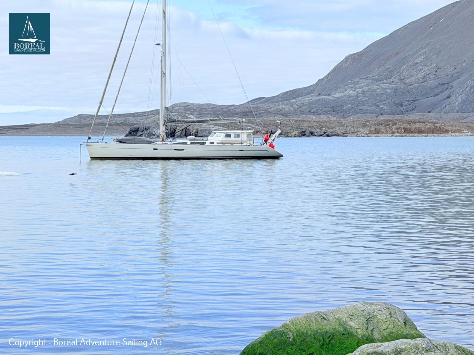Sail & Kayak, Svalbard: sailing yacht at anchor in a calm bay, mountain slopes behind