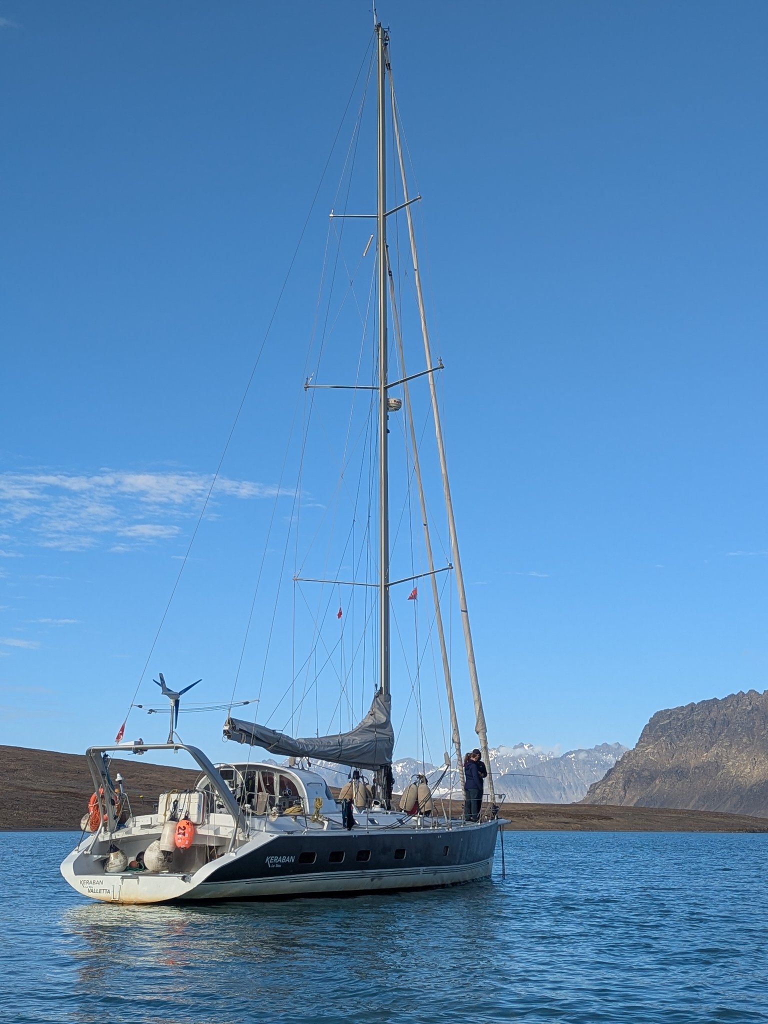 Sail & Explore, Svalbard: dark-hulled sailing yacht at anchor under blue sky, seen from the stern quarter