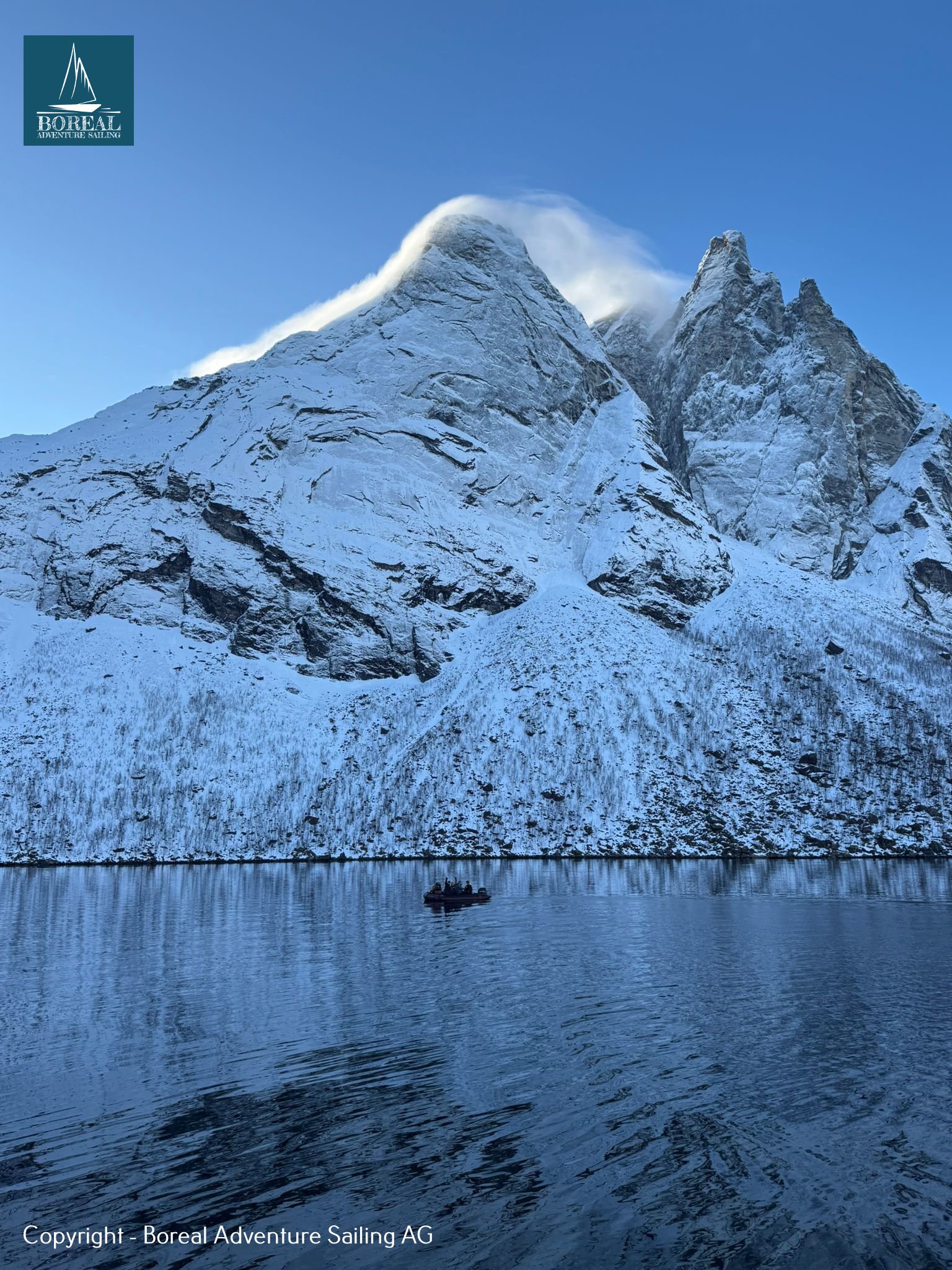 Ski & Sail, Bodø & Lofoten: snow plume blowing off a jagged peak above the fjord