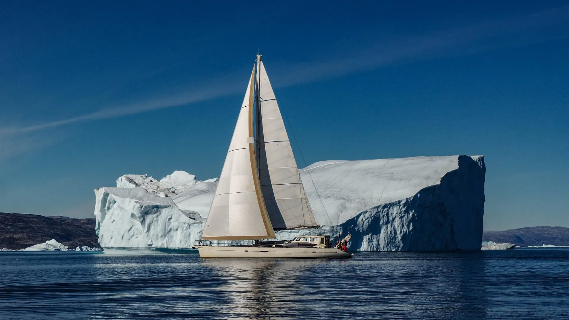 Voile & Exploration, Groenland de l’Est : le voilier toutes voiles dehors devant un iceberg tabulaire