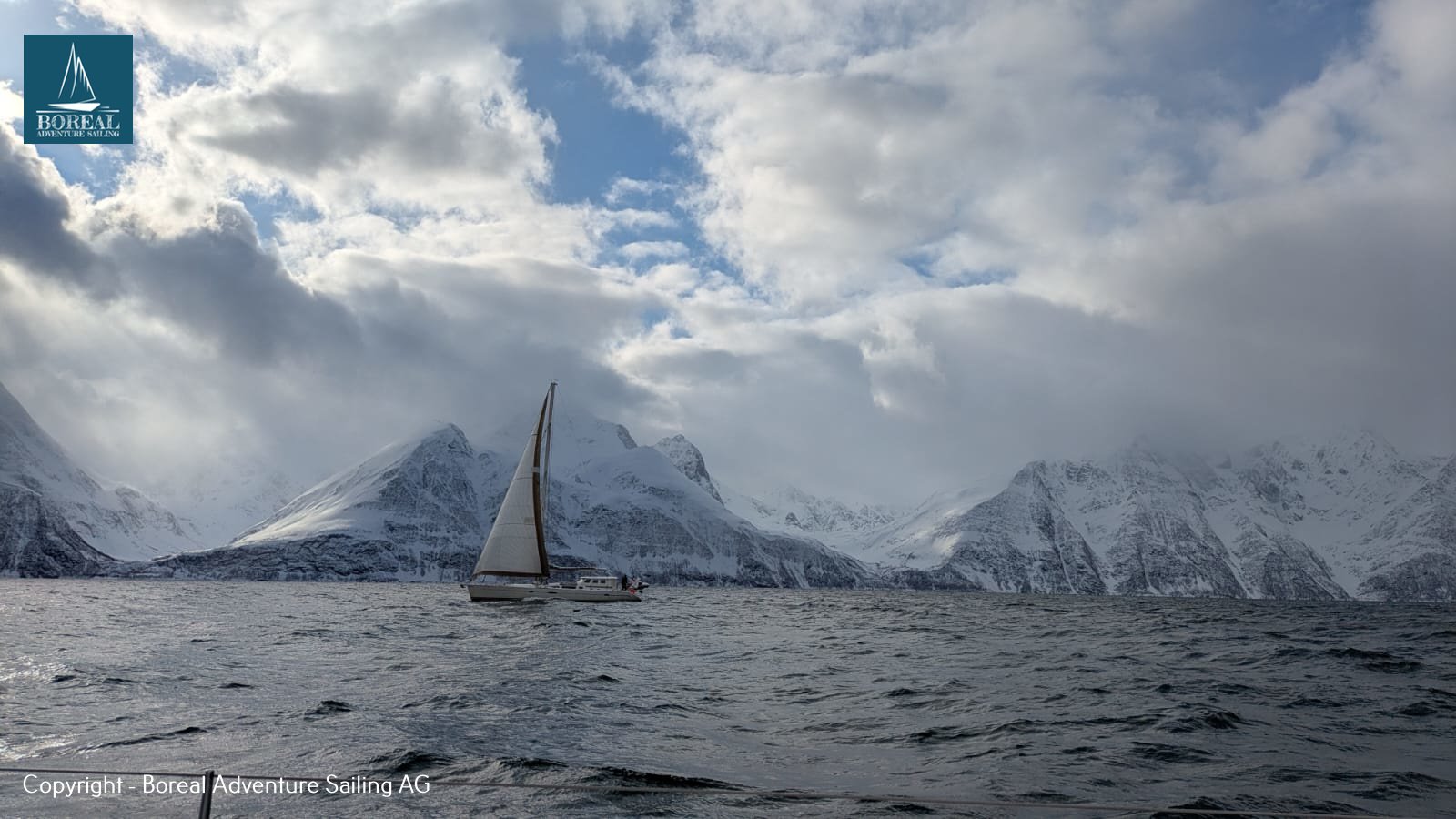 Ski & Sail, Lyngen Alps: yacht under sail beneath cloud-wrapped snowy peaks