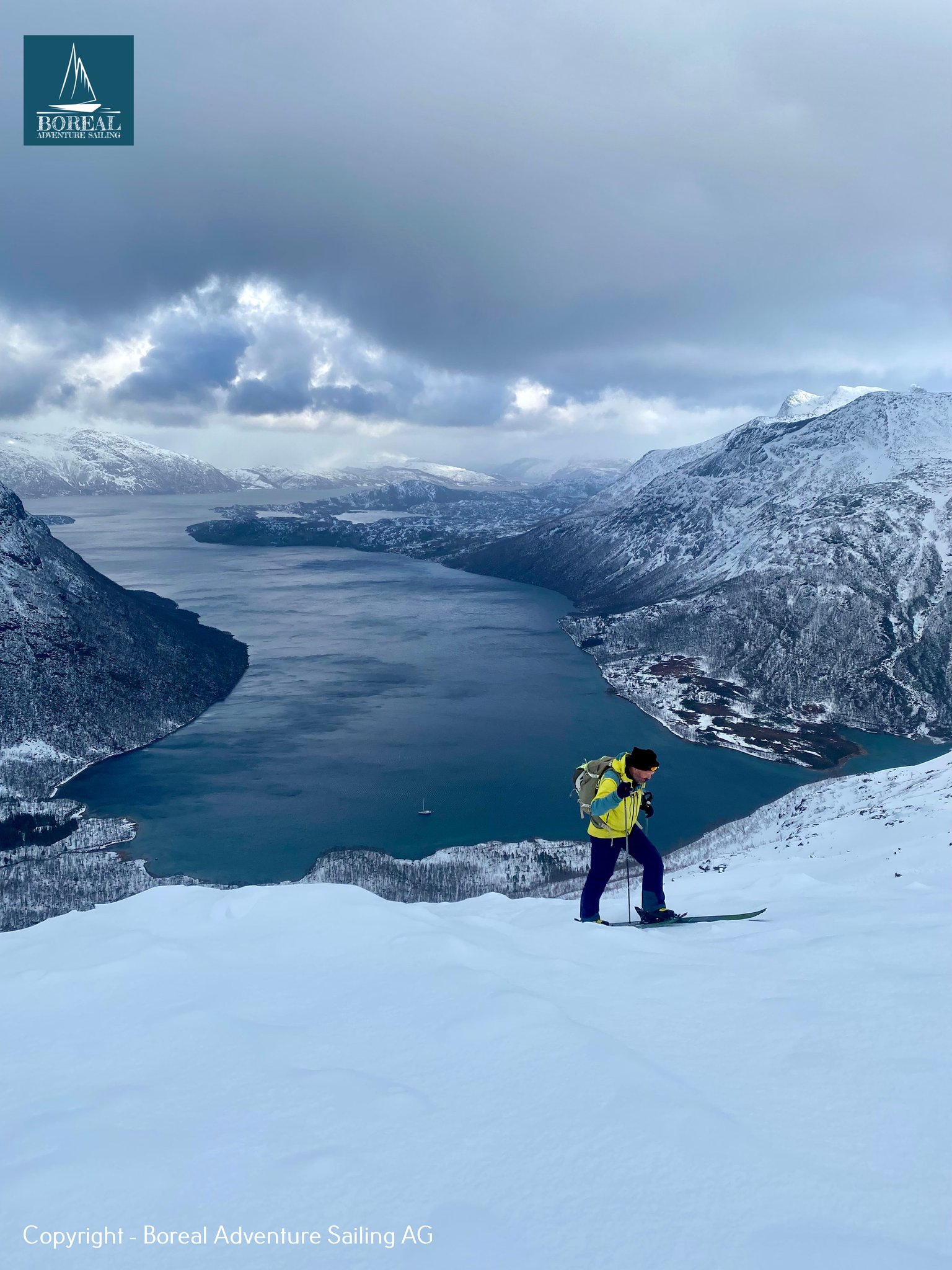 Ski & Sail, Bodø & Lofoten: ski tourer in yellow jacket on a snowy ridge above a fjord