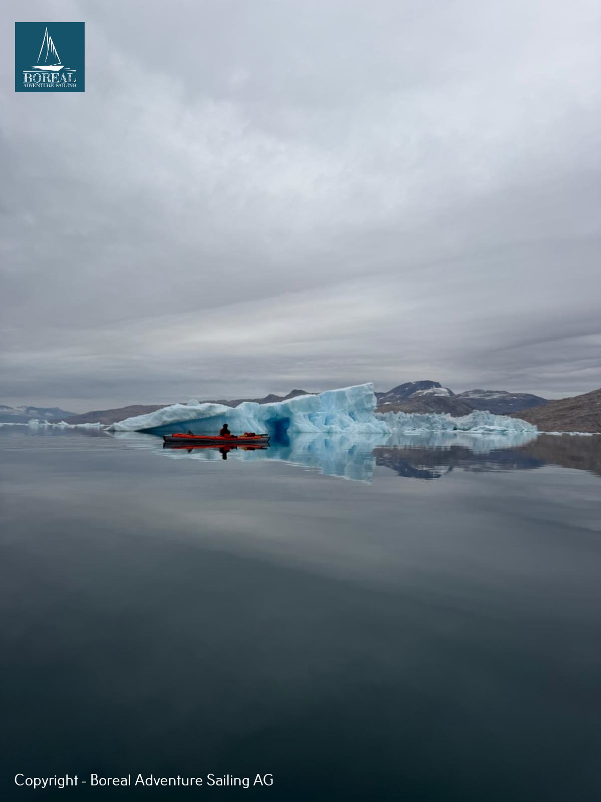 Sail & Kayak, East Greenland: lone red kayak before a blue iceberg on mirror-calm water
