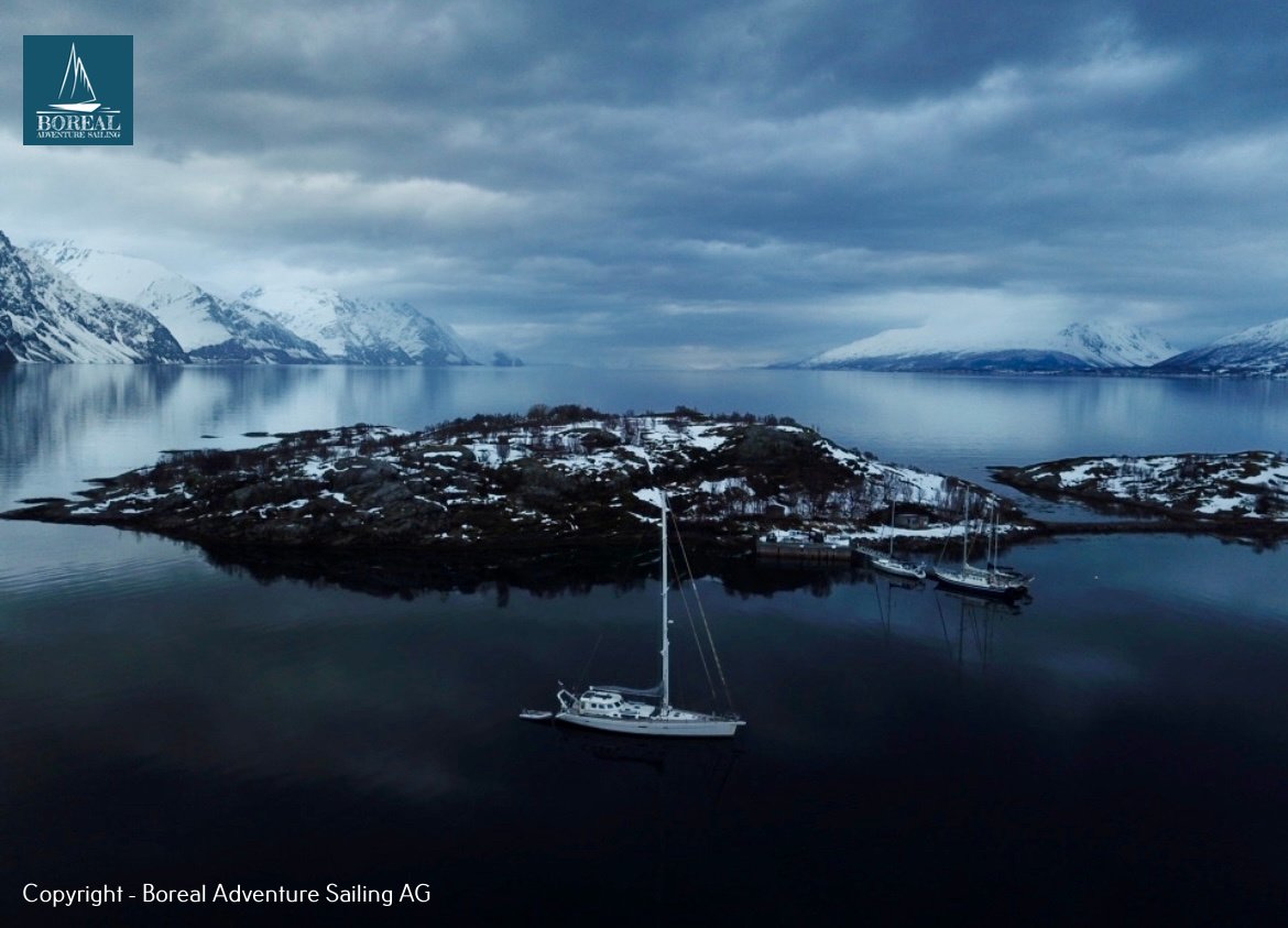 Ski & Sail, Lyngen Alps: drone view of the yacht anchored beside a snowy rocky island