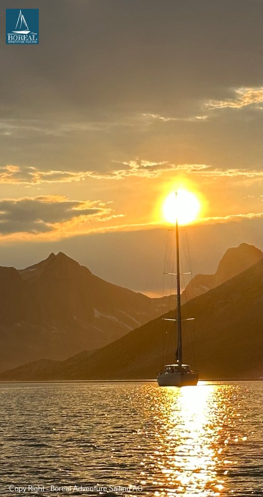 Sail & Explore, East Greenland: golden sunset behind the yacht, framed by mountain silhouettes
