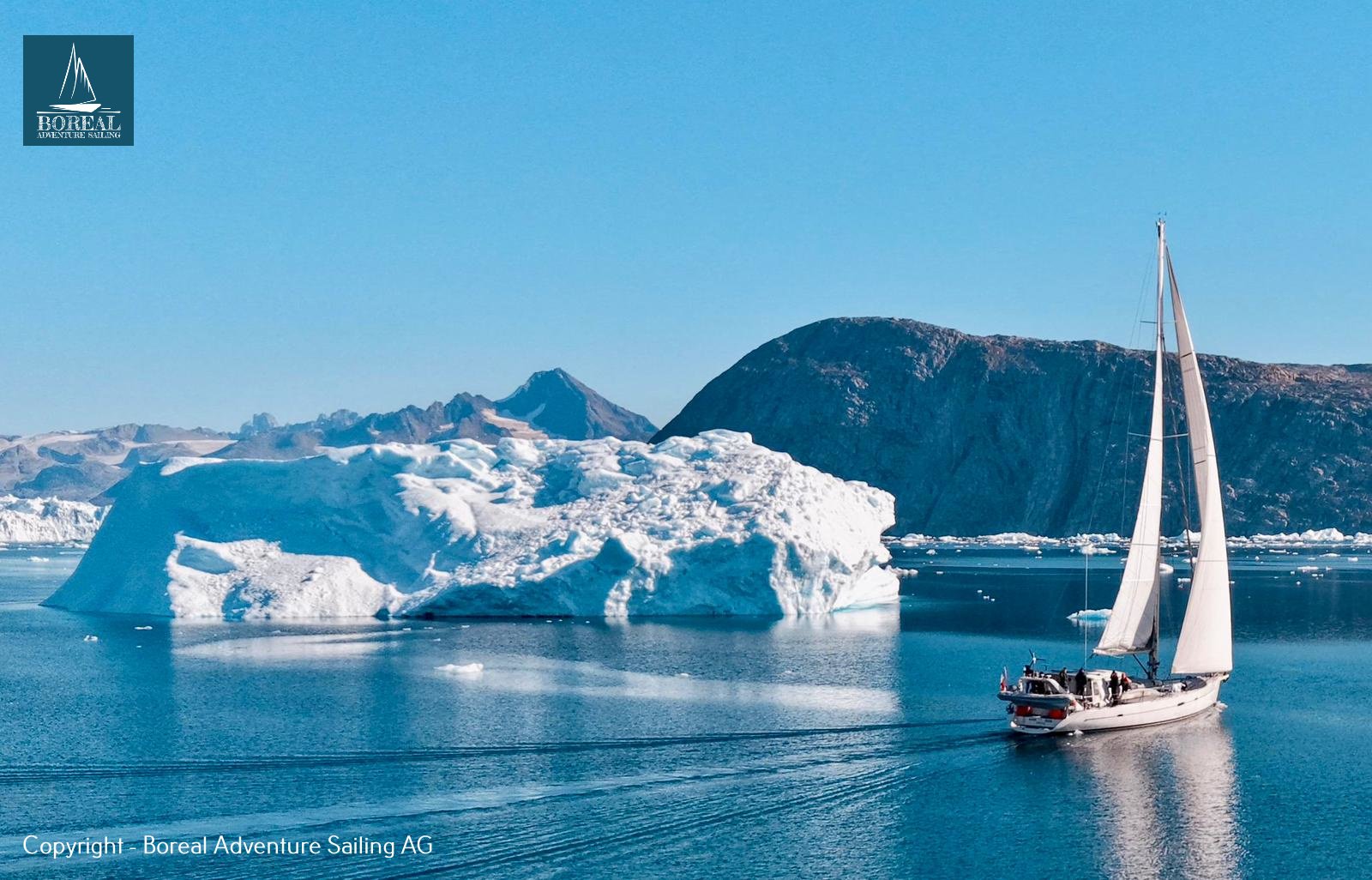 Sail & Explore, East Greenland: sailing yacht under full sail beside a large iceberg