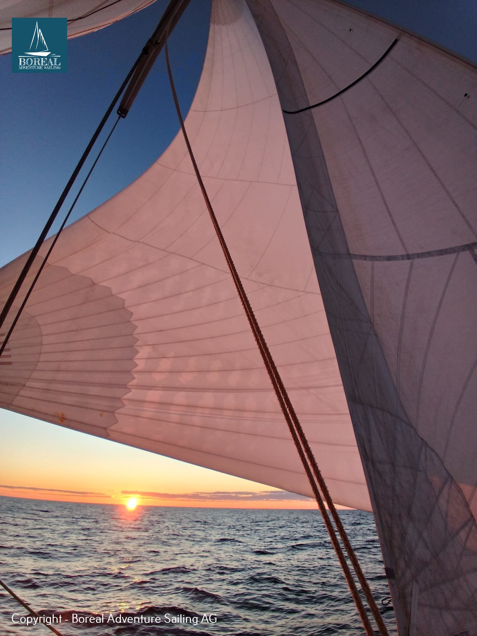 Offshore Sailing: headsail glowing pink as the sun touches the sea horizon