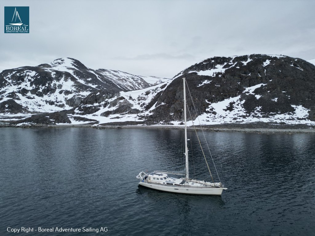Sail & Explore, Svalbard: drone view of the yacht at anchor below snow-patched mountains