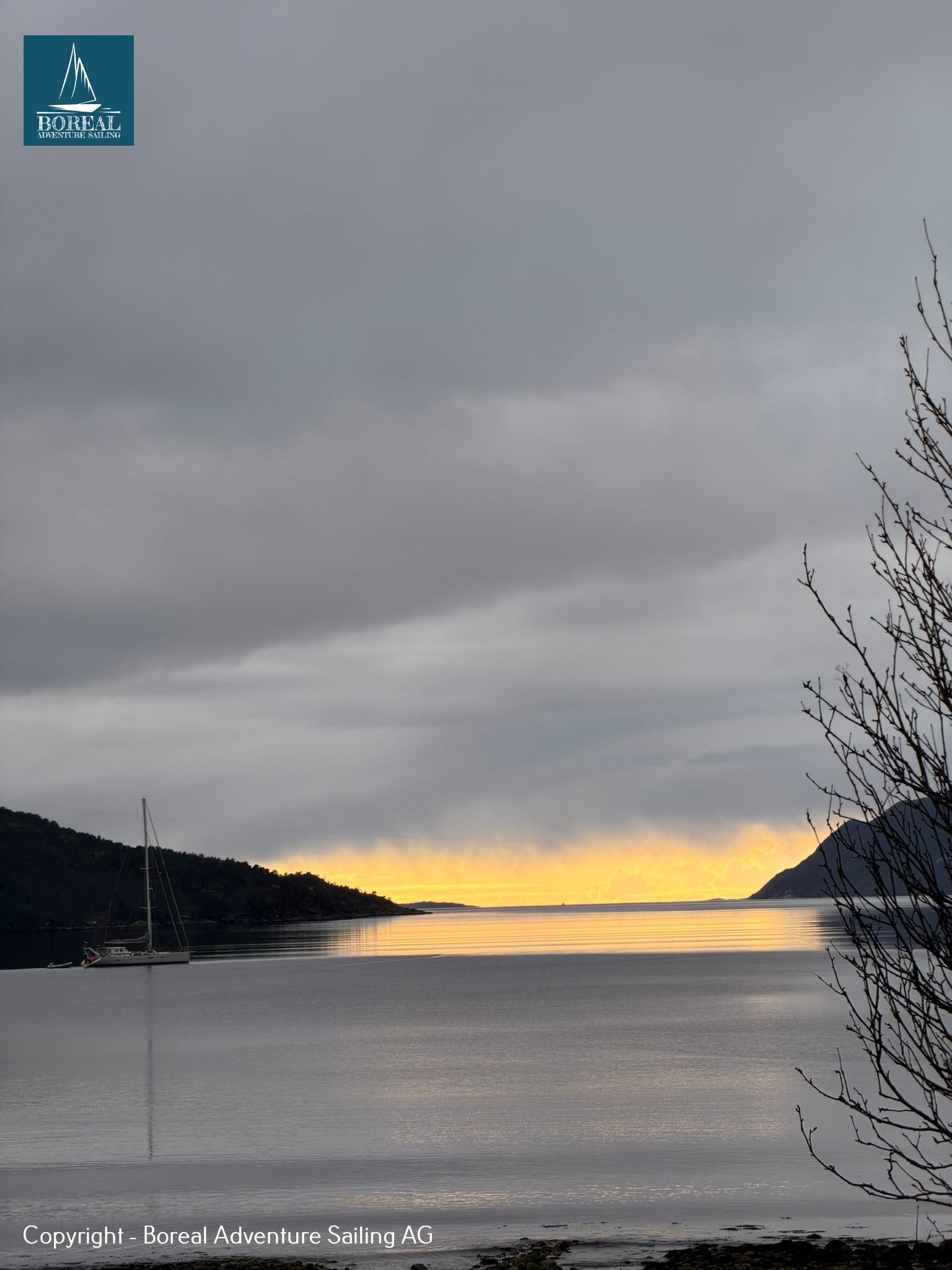 Ski & Sail, Bodø & Lofoten: golden horizon glow over a fjord with a yacht at anchor