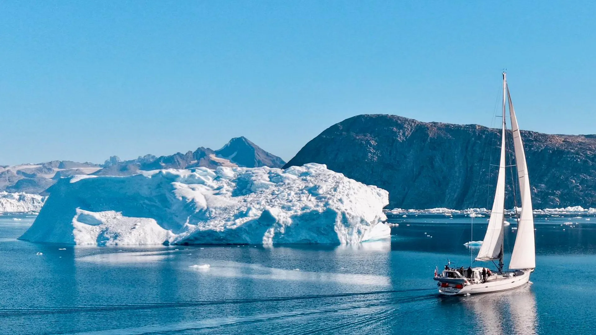 Voile & Exploration, Groenland de l’Est : le voilier sous voiles à côté d’un grand iceberg