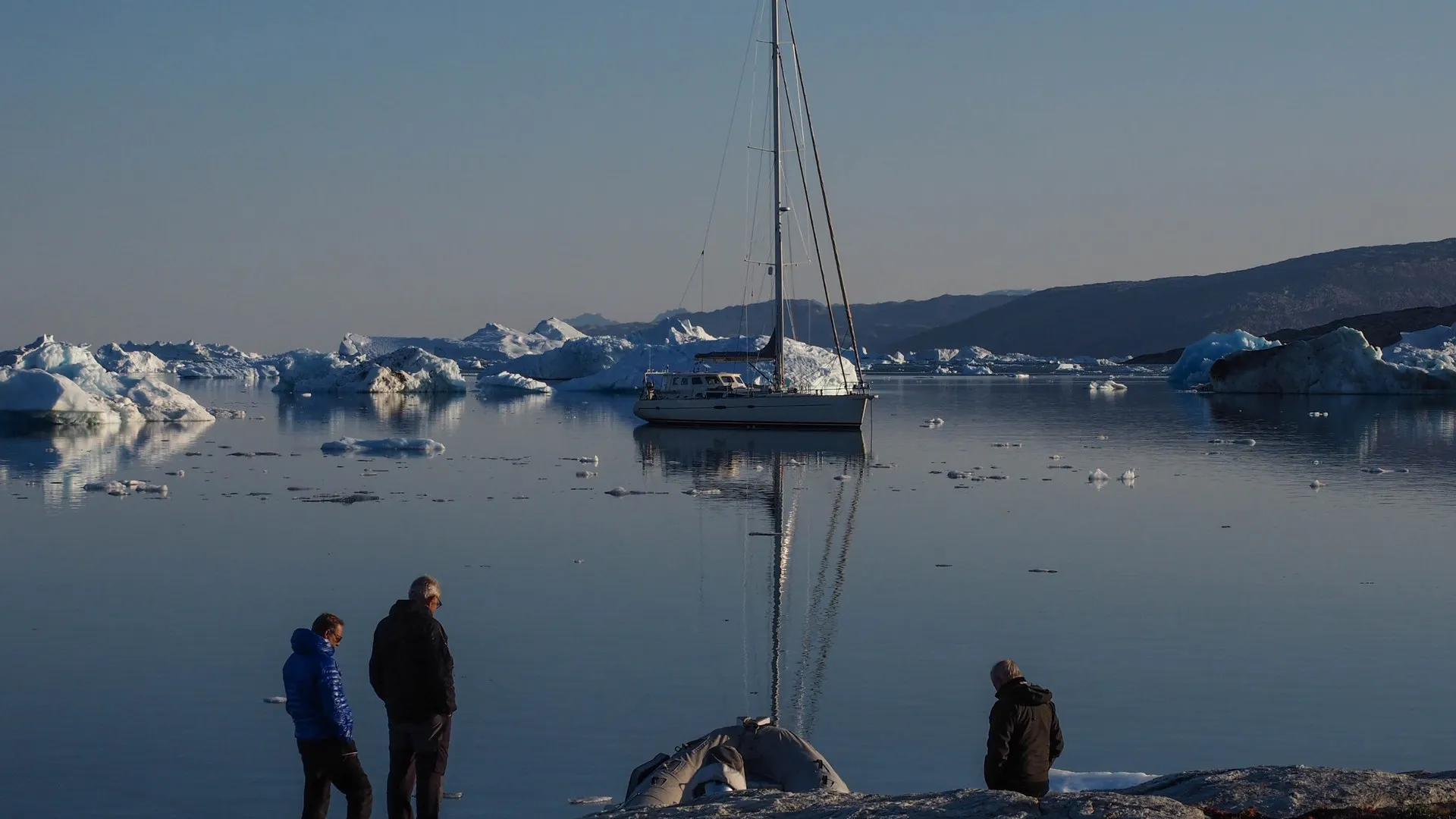Voile & Exploration, Groenland de l’Est : participants sur le rivage regardant le voilier au mouillage parmi les icebergs