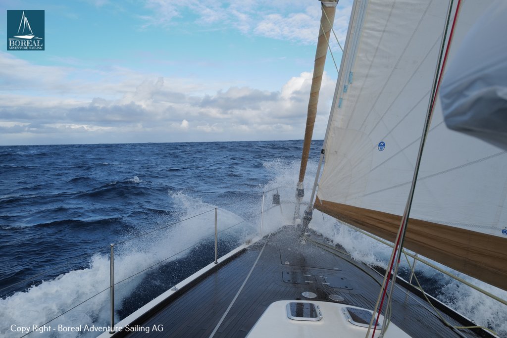 Offshore Sailing: yacht heeling under sail, bow wave spraying across deep blue sea