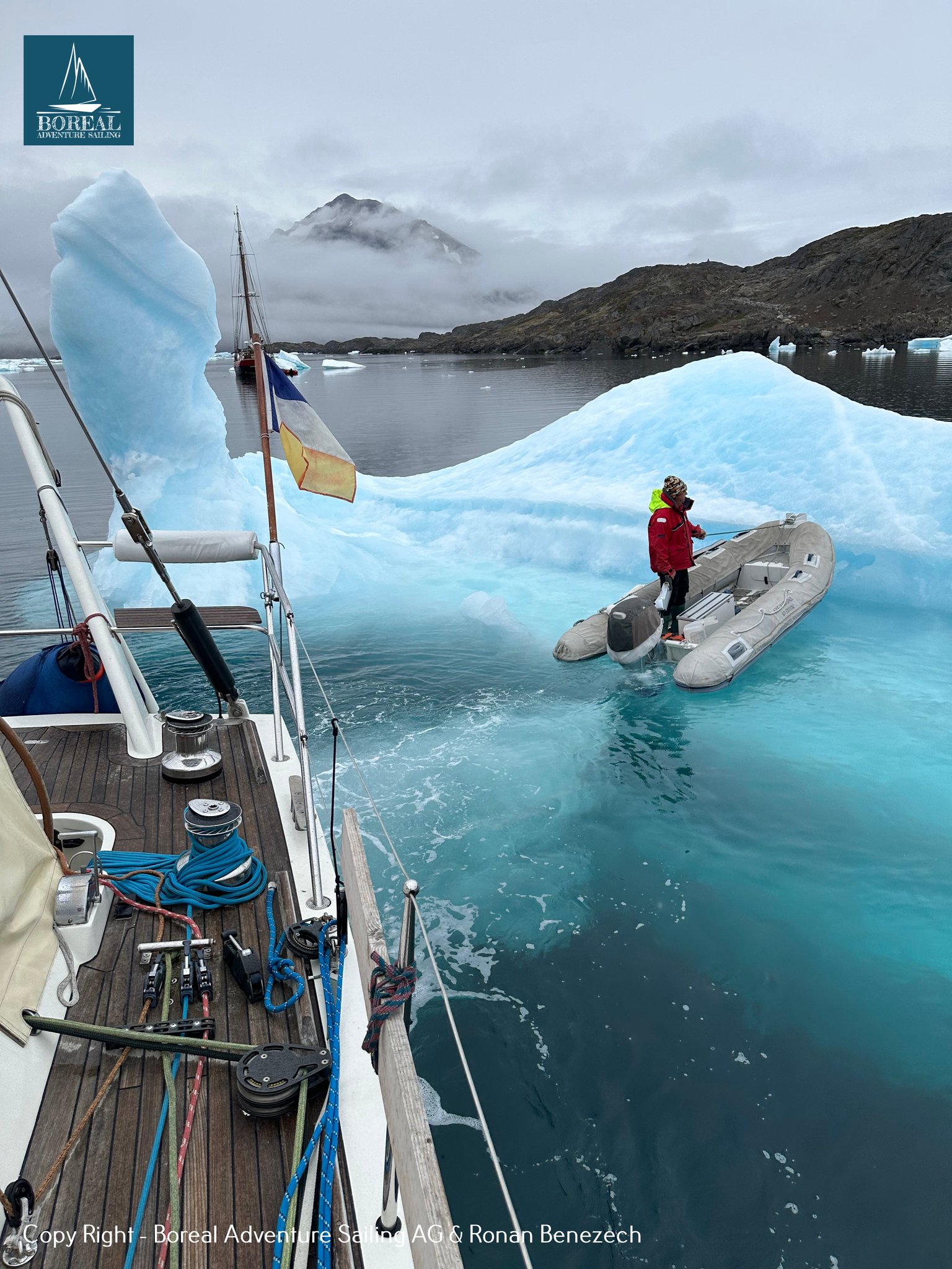 Sail & Explore, East Greenland: dinghy excursion beside a turquoise iceberg, seen from the deck