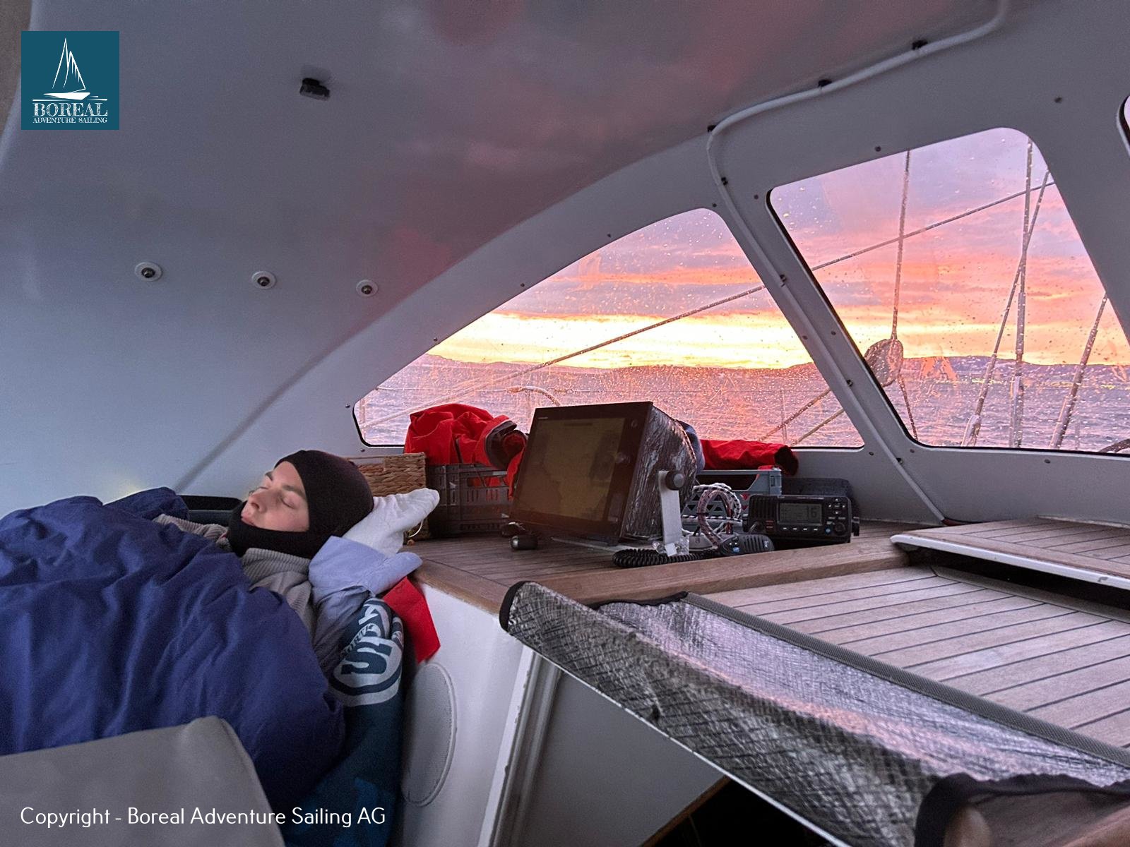 Offshore Sailing: off-watch crew resting in the doghouse under a pink sky