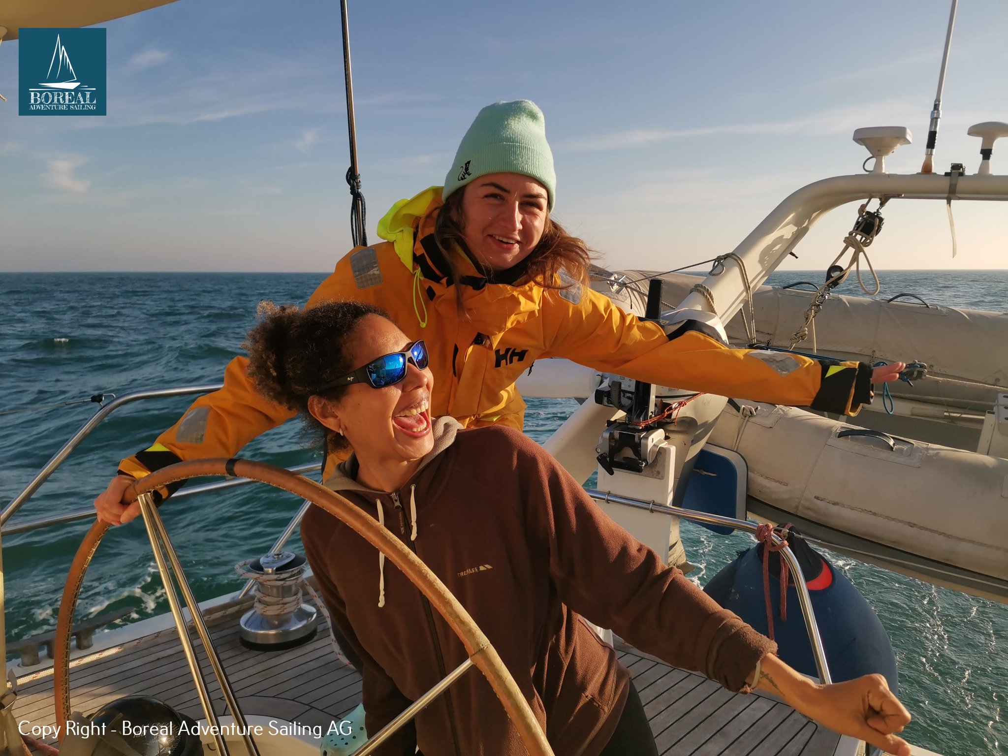Offshore Sailing: two smiling crew members sharing the helm in warm sunlight