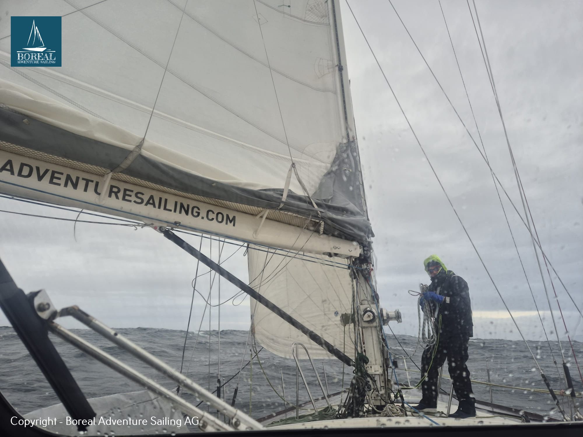 Offshore Sailing: crew working at the mast beneath the mainsail on grey seas