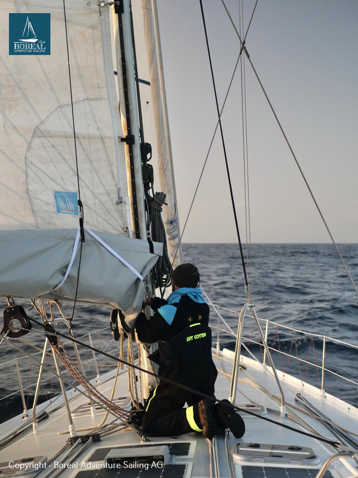 Offshore Sailing: crew kneeling on the foredeck handling a sail at sea