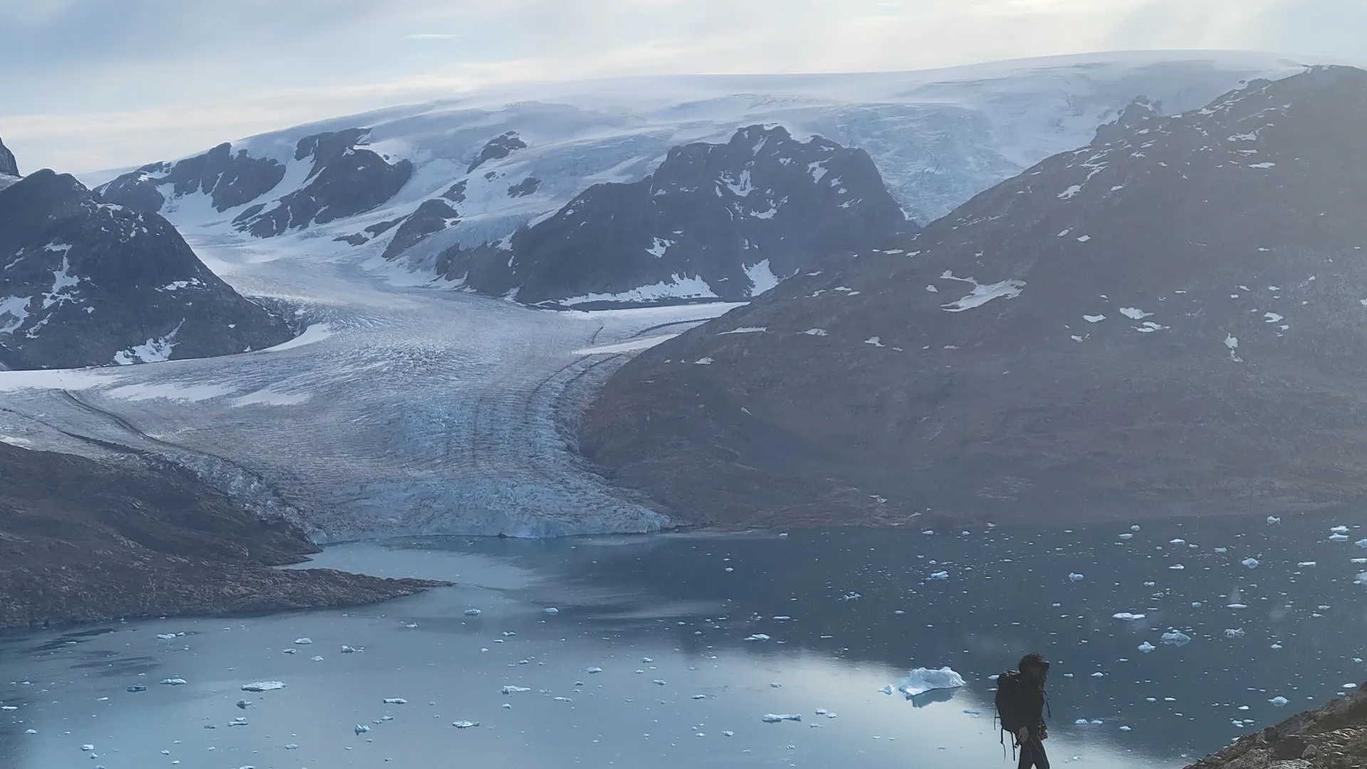 Voile & Exploration, Groenland de l’Est : randonneur au-dessus d’un fjord face à un glacier descendant de la calotte glaciaire