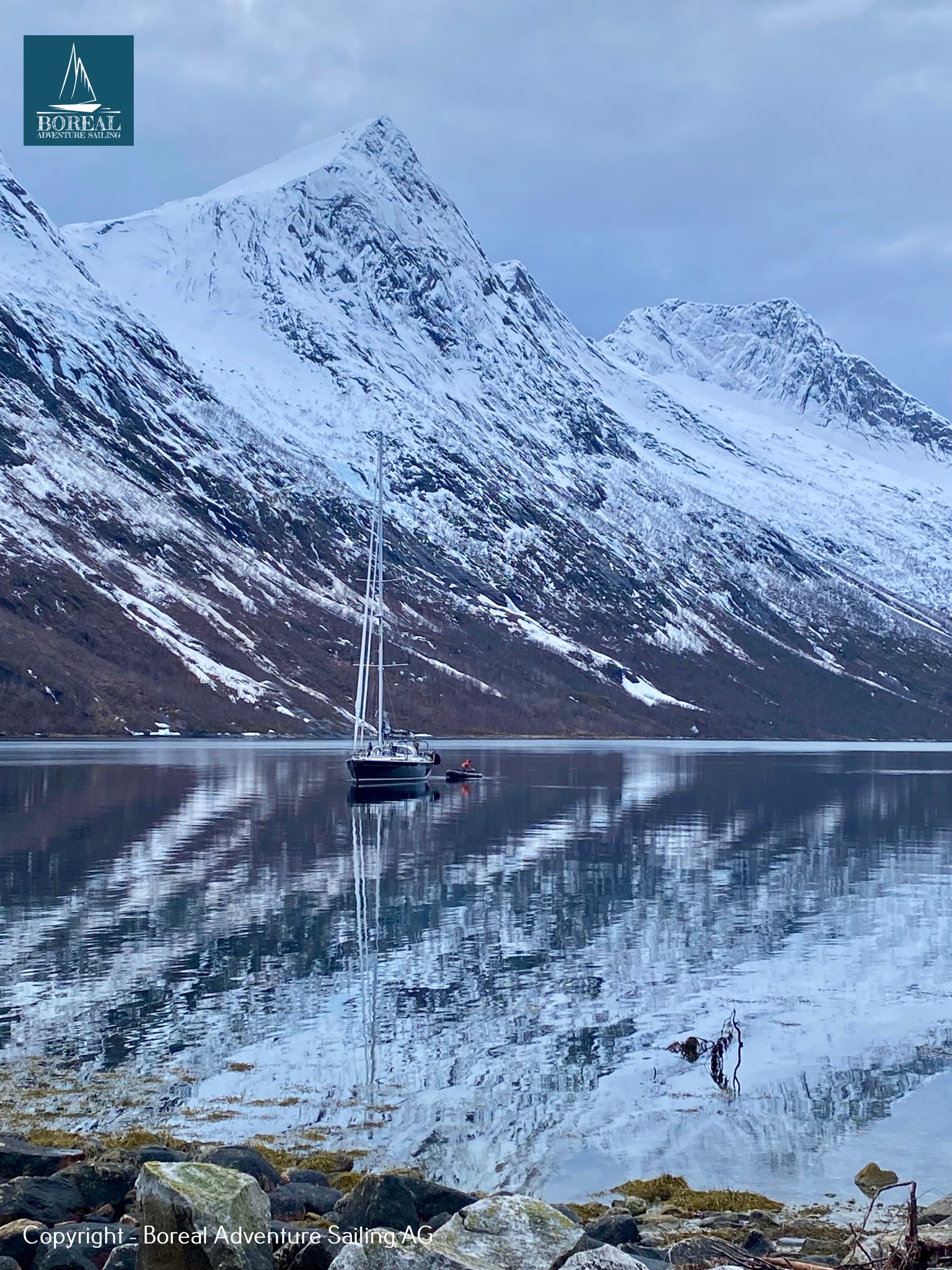 Ski & Sail, Bodø & Lofoten: sailing yacht anchored beneath a steep snowy peak, reflected in the fjord