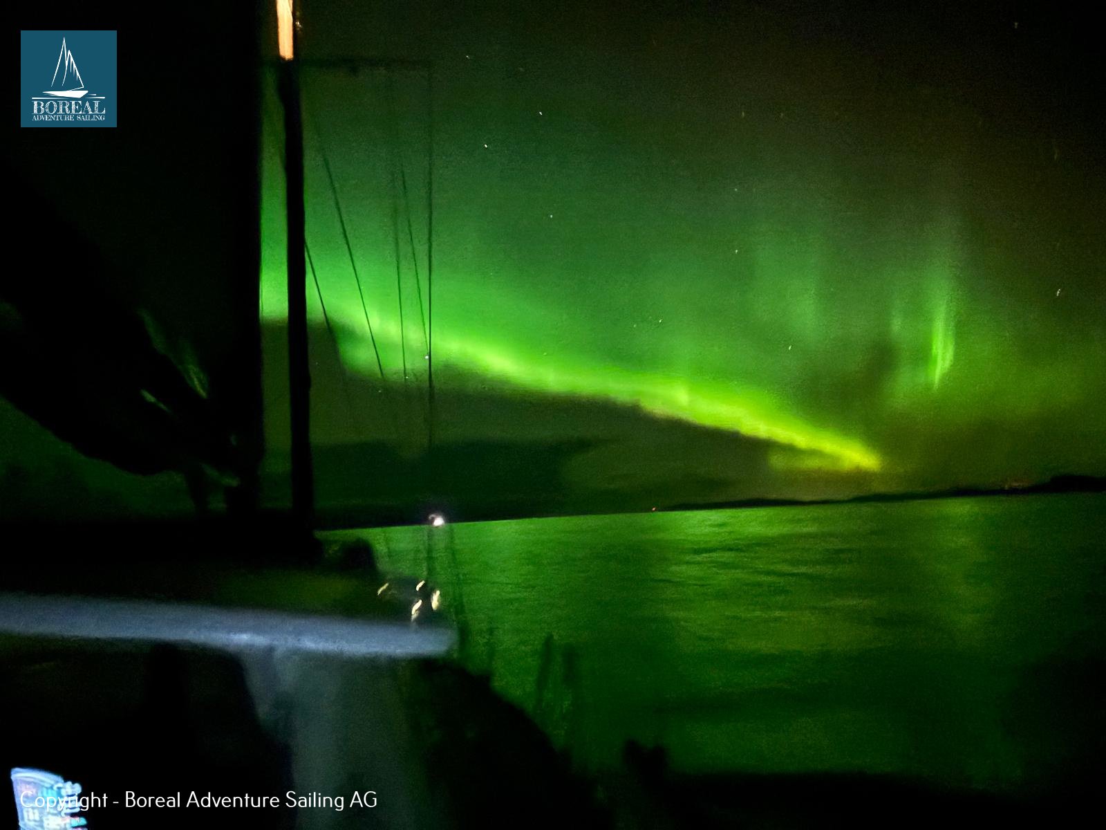 Offshore Sailing: green northern lights reflected in calm water beside the yacht