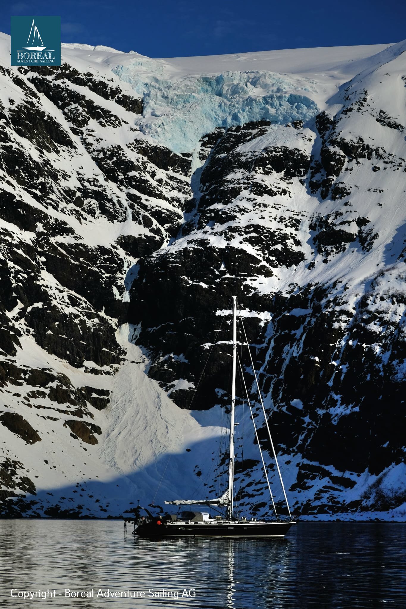Ski & Sail, Lyngen Alps: yacht at anchor below steep cliffs and a hanging glacier