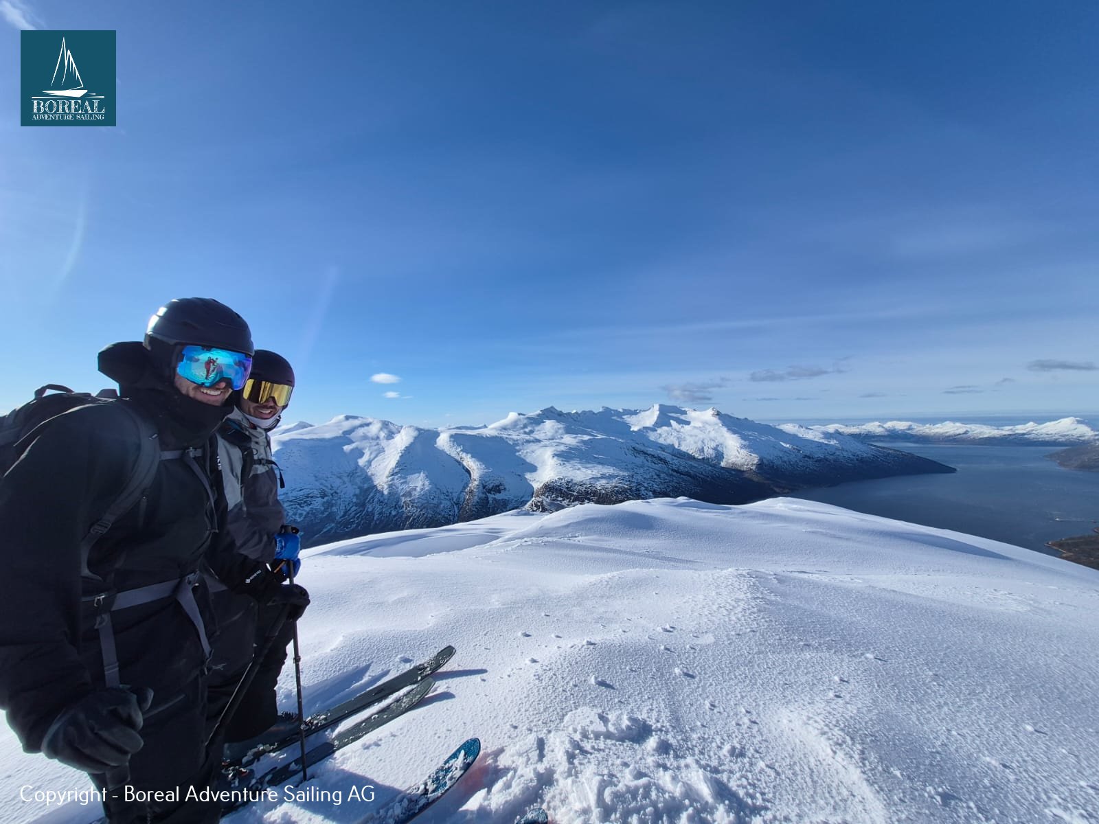Ski & Sail, Bodø & Lofoten: two skiers in goggles on a summit overlooking mountains and sea