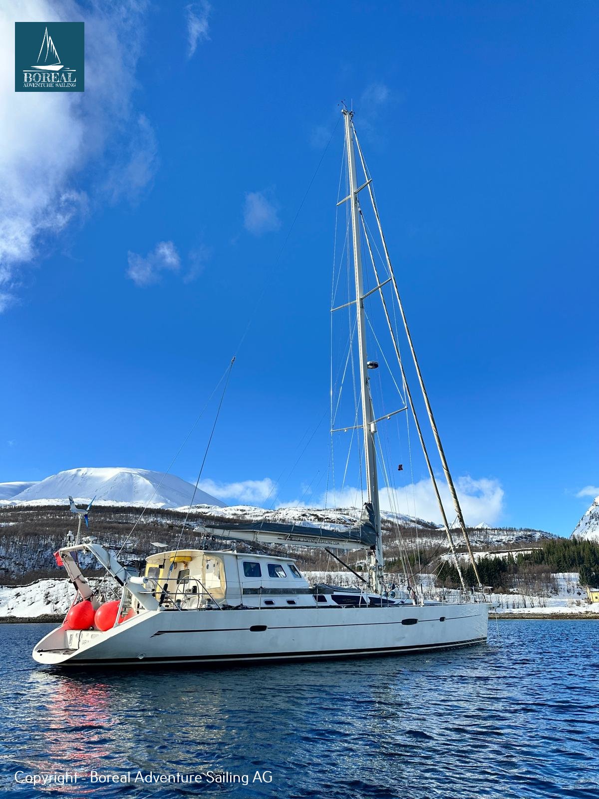 Ski & Sail, Lyngen Alps: white sailing yacht at anchor off a snowy shore under blue sky