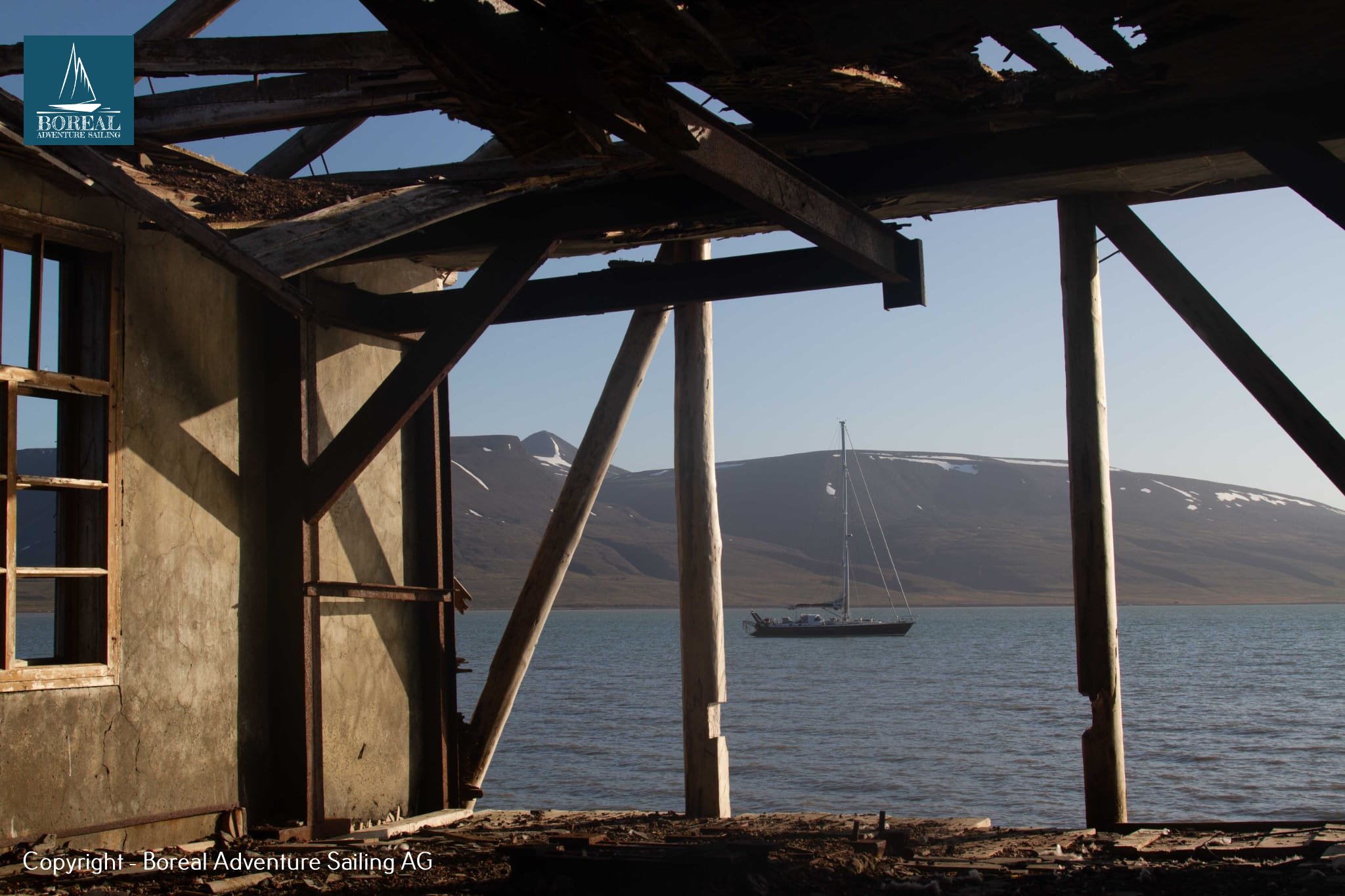 Sail & Explore, Svalbard: anchored yacht framed by the timbers of an abandoned building