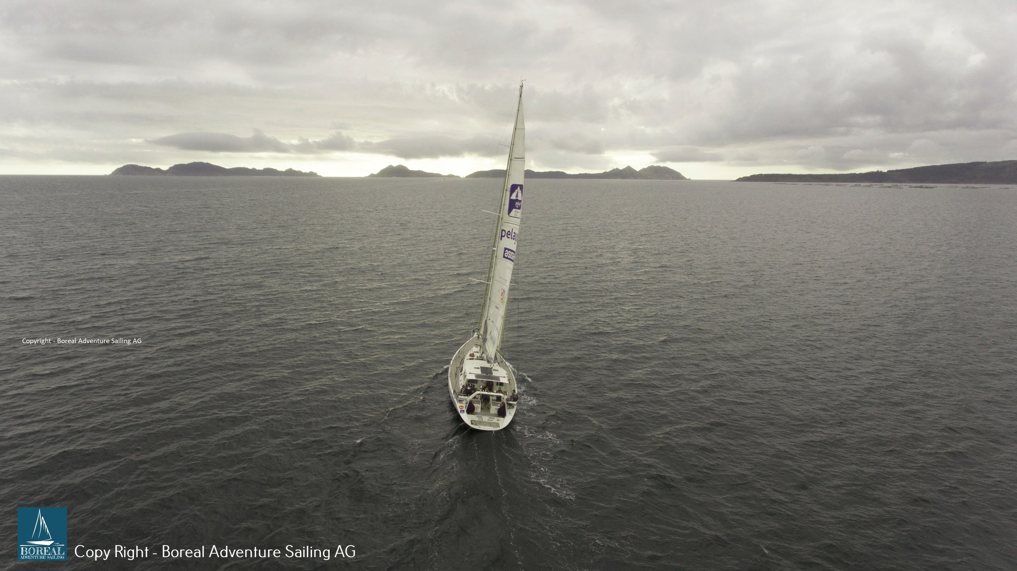 Offshore Sailing: drone view from astern of the yacht heading for a distant coast under grey skies